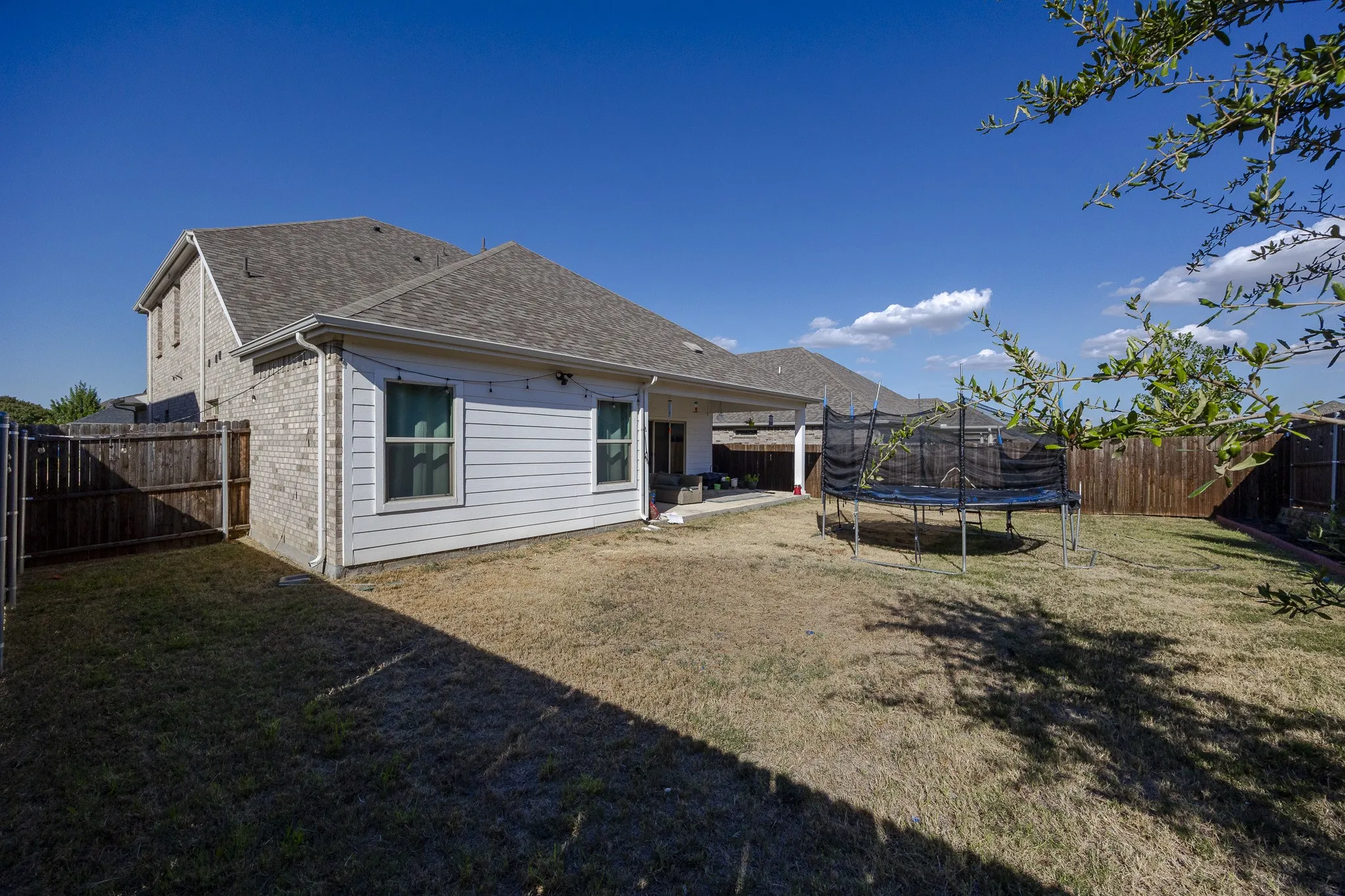 Expansive backyard featuring a covered patio, privacy fencing, and a two-story exterior with brick and siding