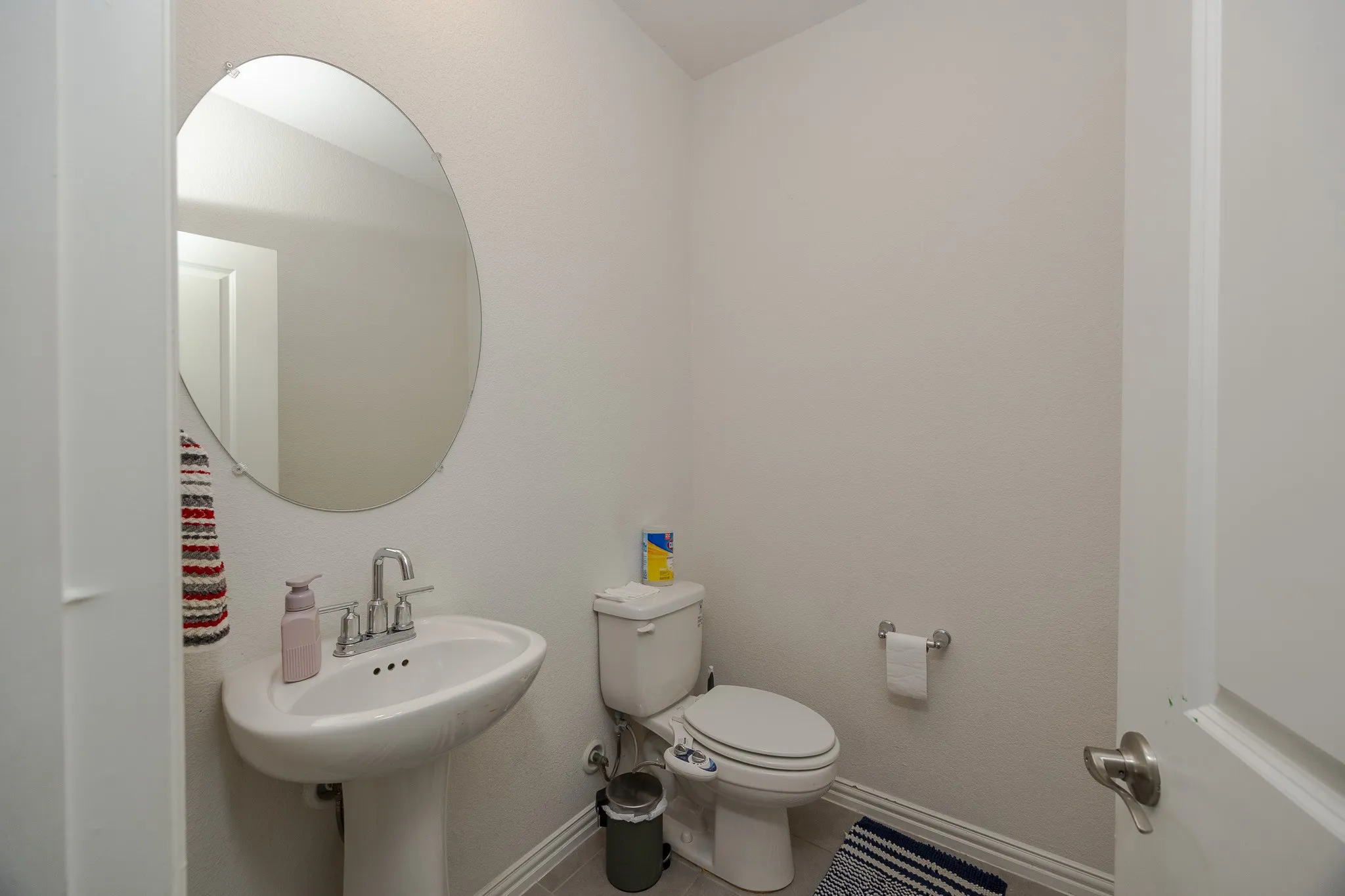 Pedestal sink with chrome faucet, oval wall mirror, and neutral wall tones