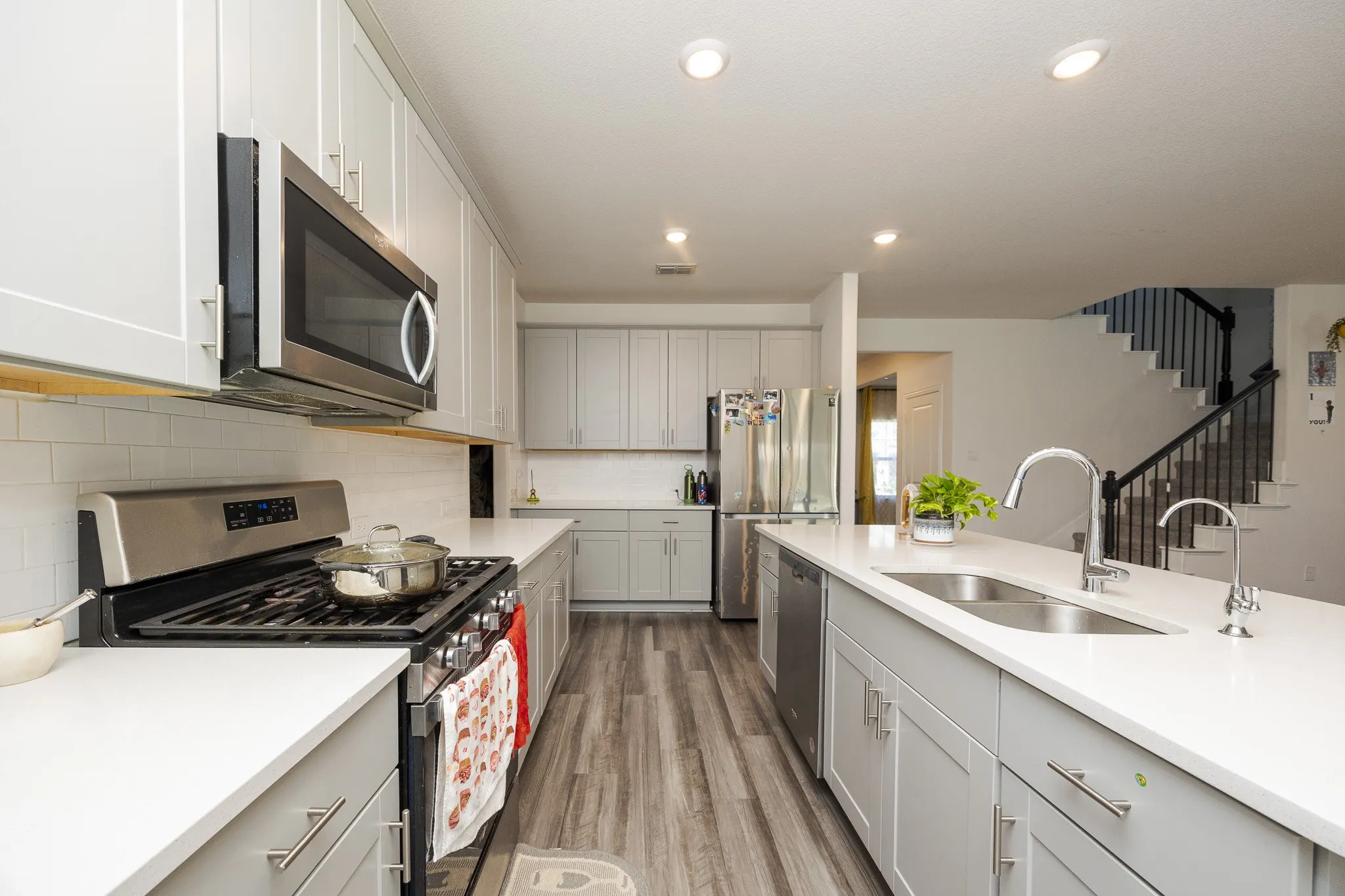 Modern kitchen featuring light gray cabinetry, white countertops, wood-finish flooring, and stainless steel appliances