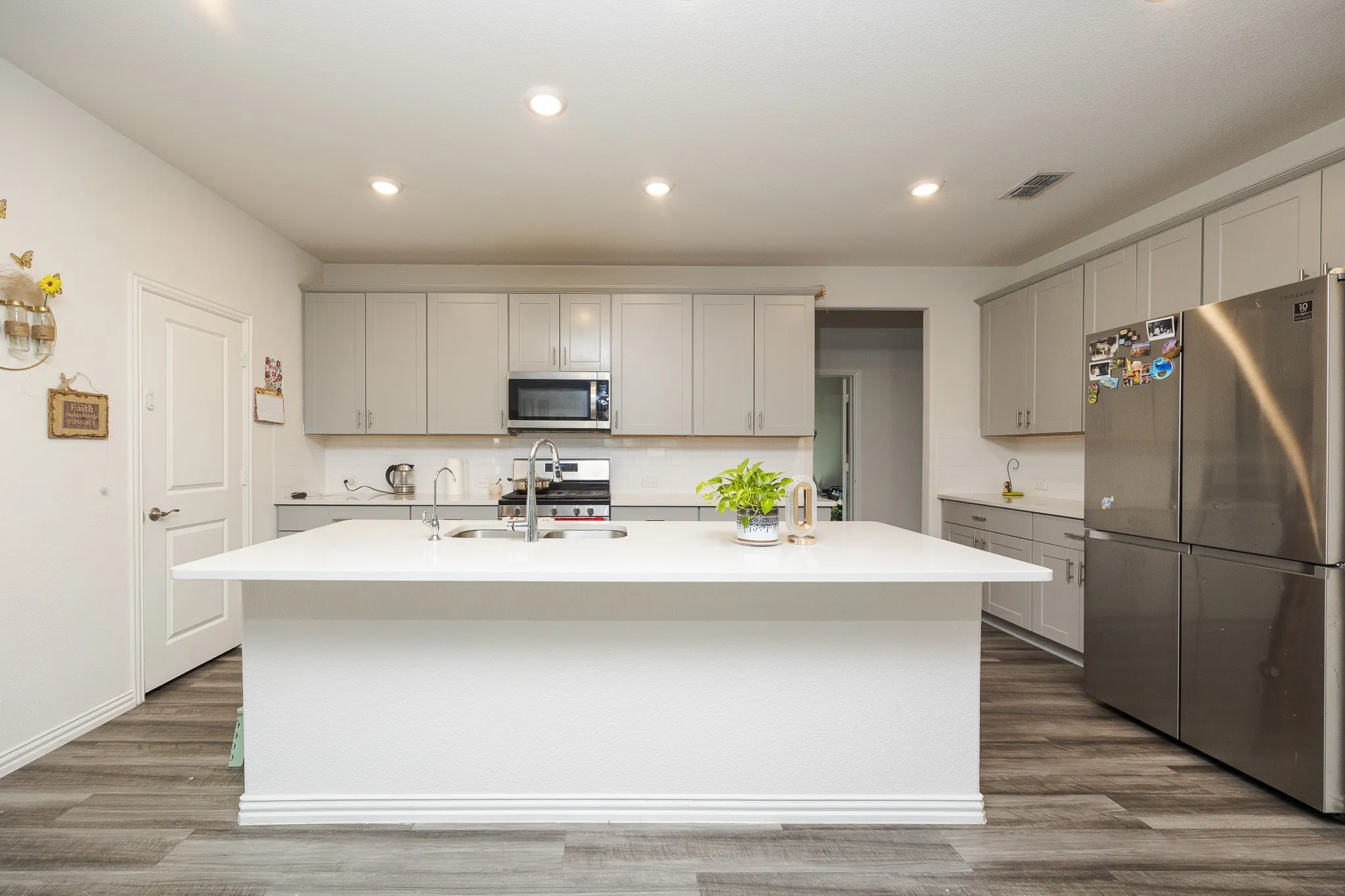 Kitchen featuring an island with a light-toned countertop, gray cabinetry, stainless steel appliances, and wood-finish flooring