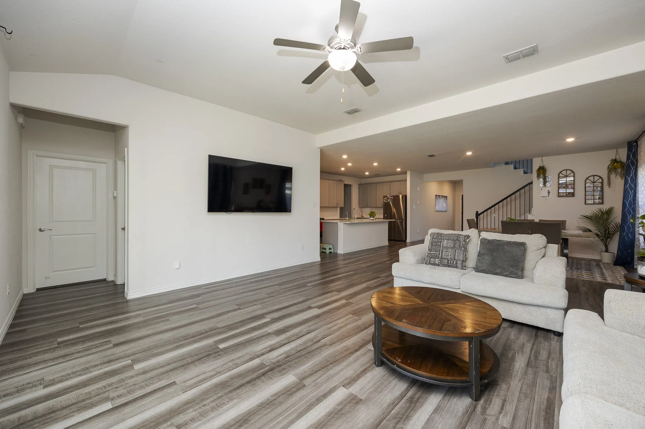 Vaulted ceiling with a ceiling fan, wood-finish flooring, recessed lighting, and a kitchen with an island featuring a breakfast bar