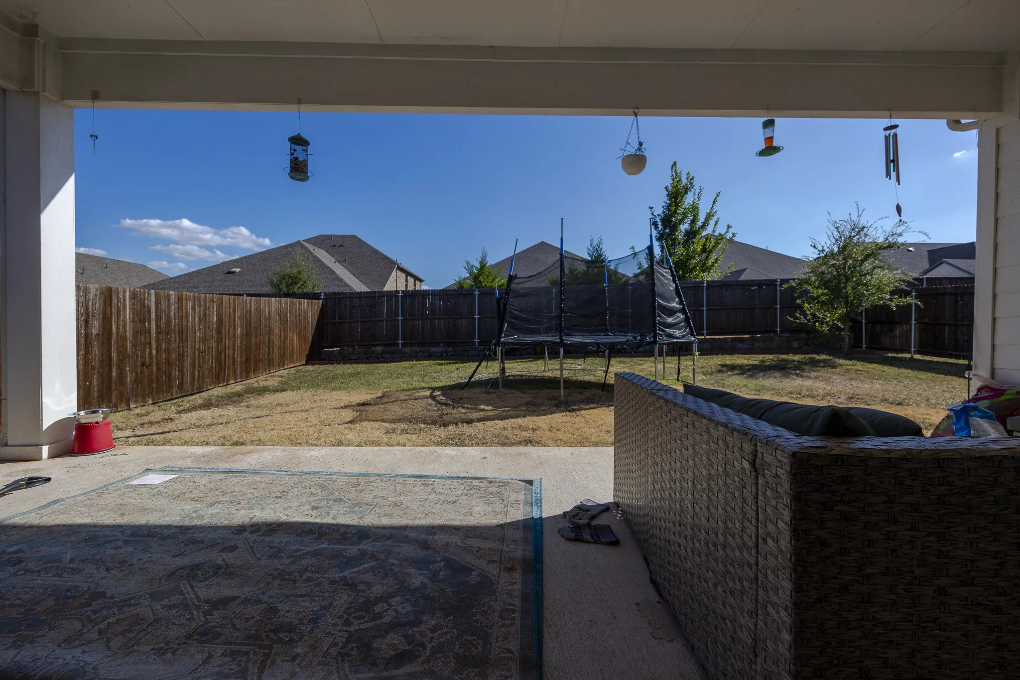 Covered patio with concrete flooring, opening to a fenced backyard with mature trees