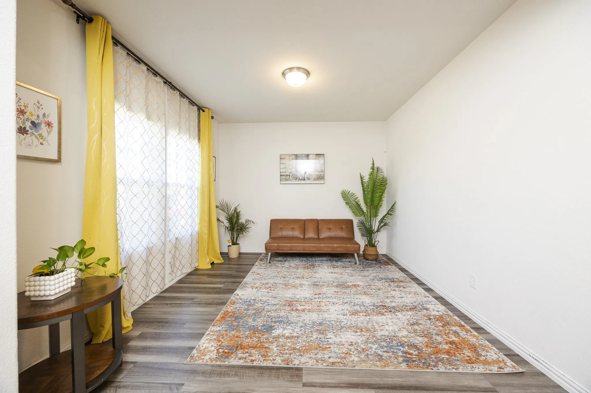 Wood-finish flooring throughout, bright white walls, and a prominent window with sheer and solid panel drapery