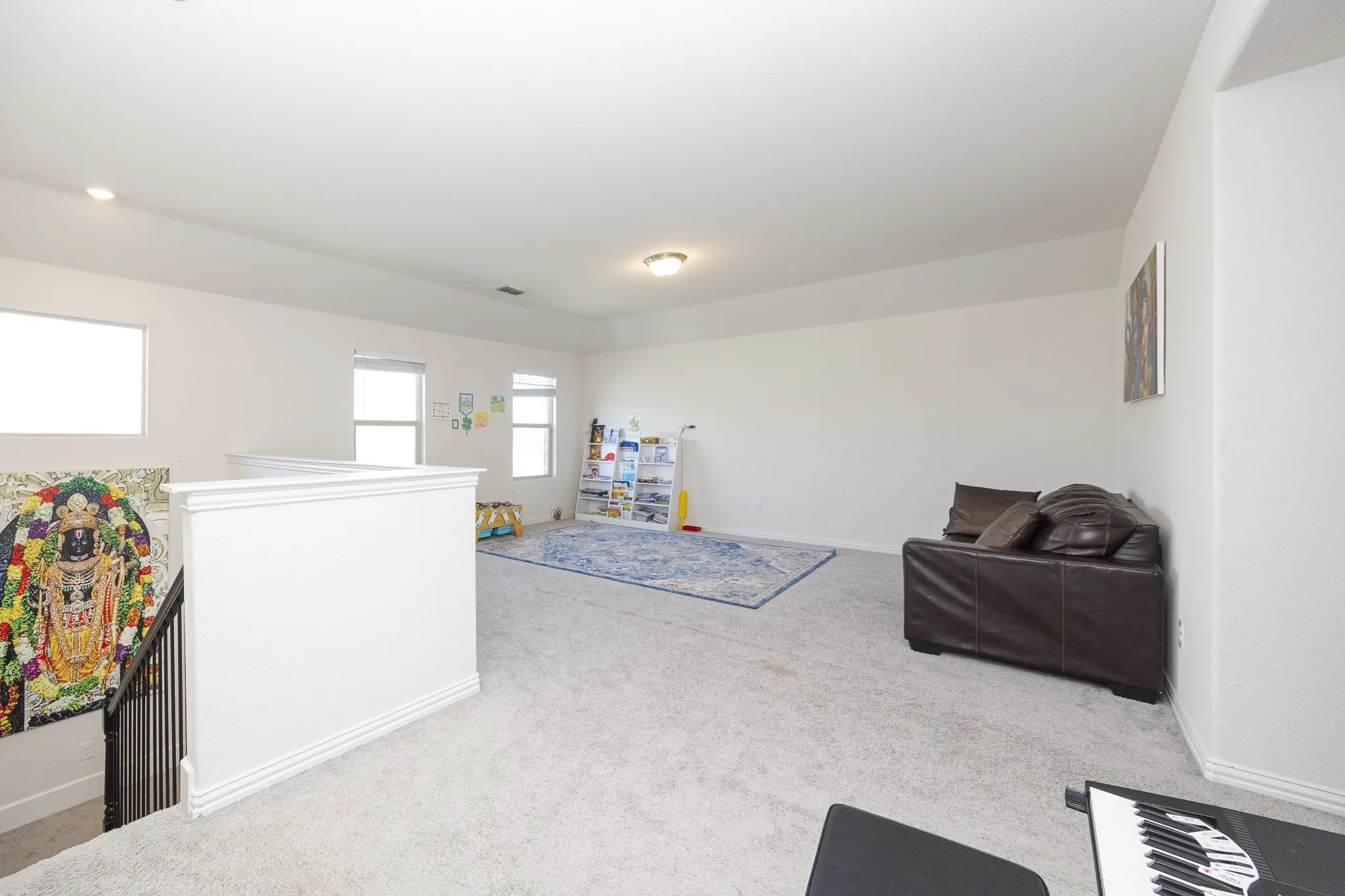 Carpeted open area with white walls, multiple windows, and a built-in staircase railing