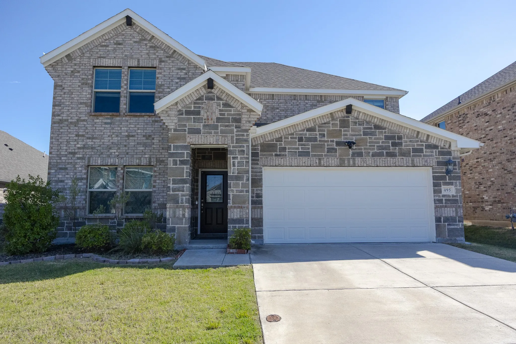Two-story exterior featuring a stone and brick facade, an attached two-car garage, and a concrete driveway