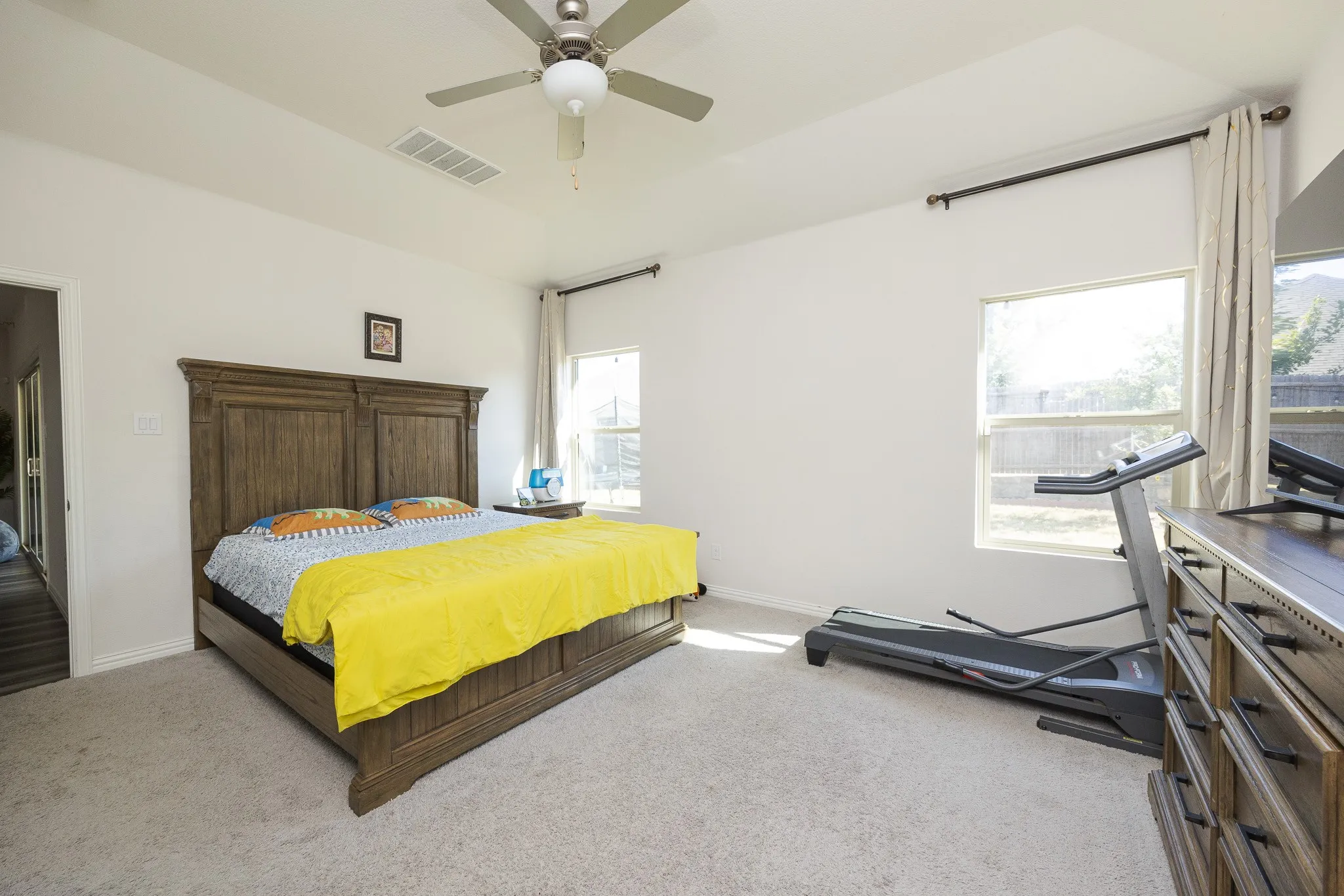 Tray ceiling with a ceiling fan, light-colored carpeting, and two windows