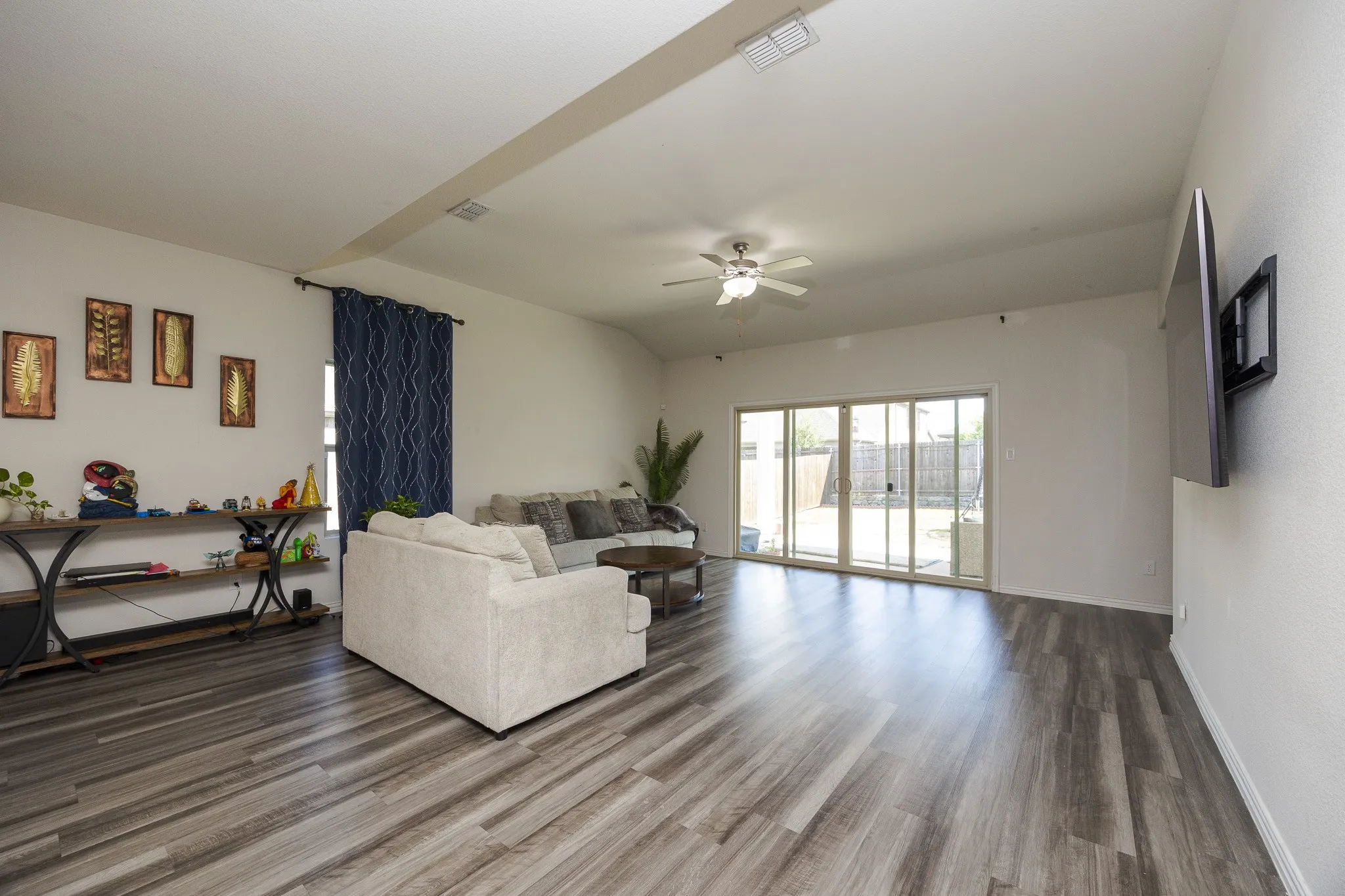 Spacious living area featuring wood-finish flooring, a ceiling fan, and sliding glass doors