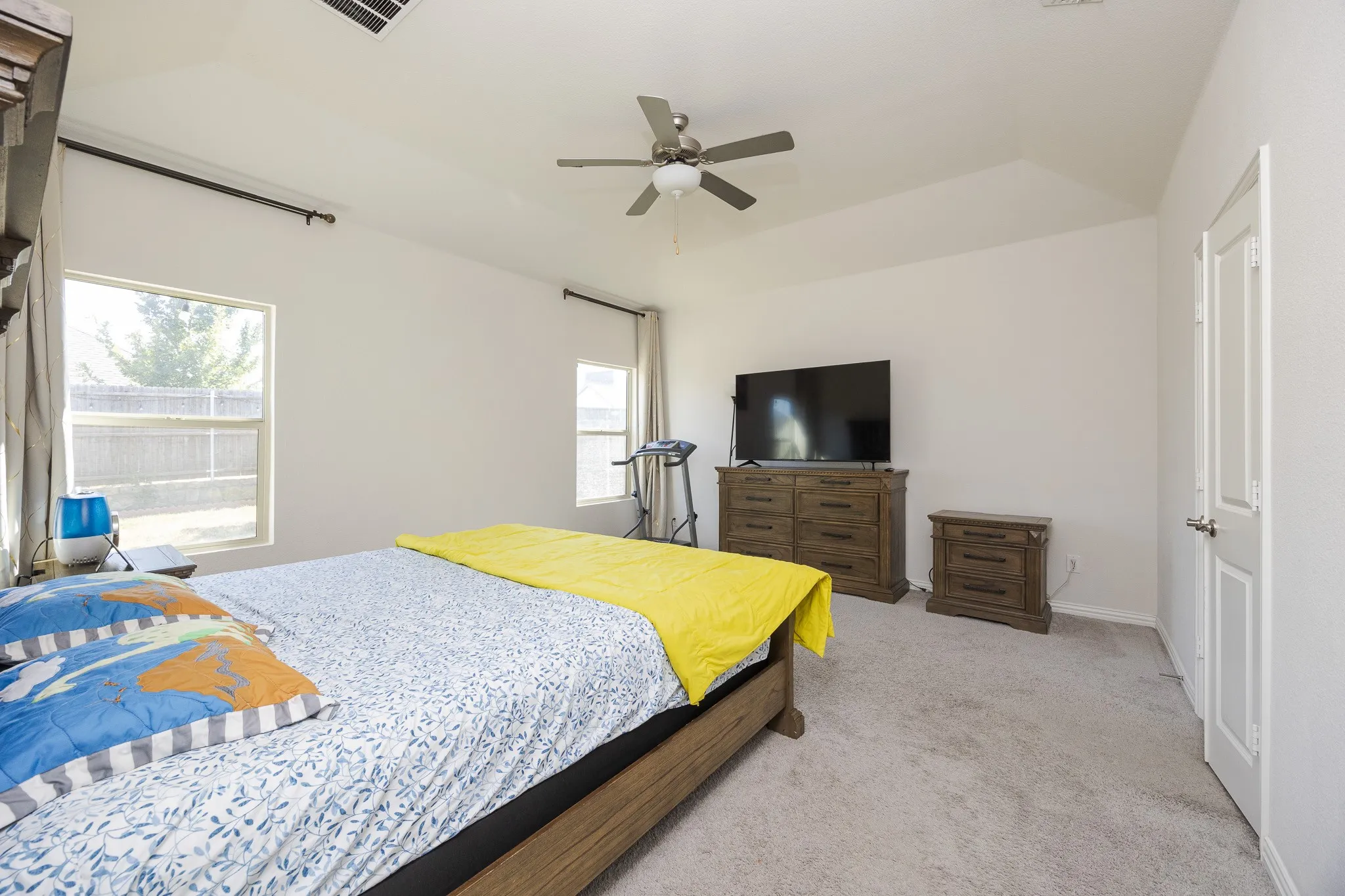 Vaulted ceiling with a ceiling fan, dual windows with curtain rods, and neutral carpet flooring