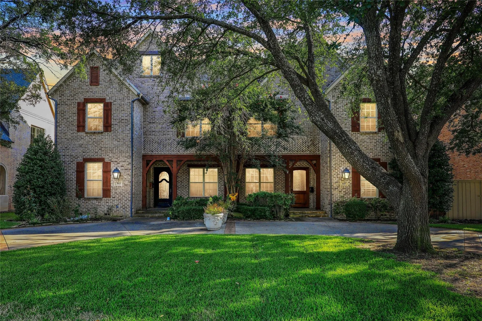 Brick exterior with contrasting wood shutters, arched entryway, and mature trees