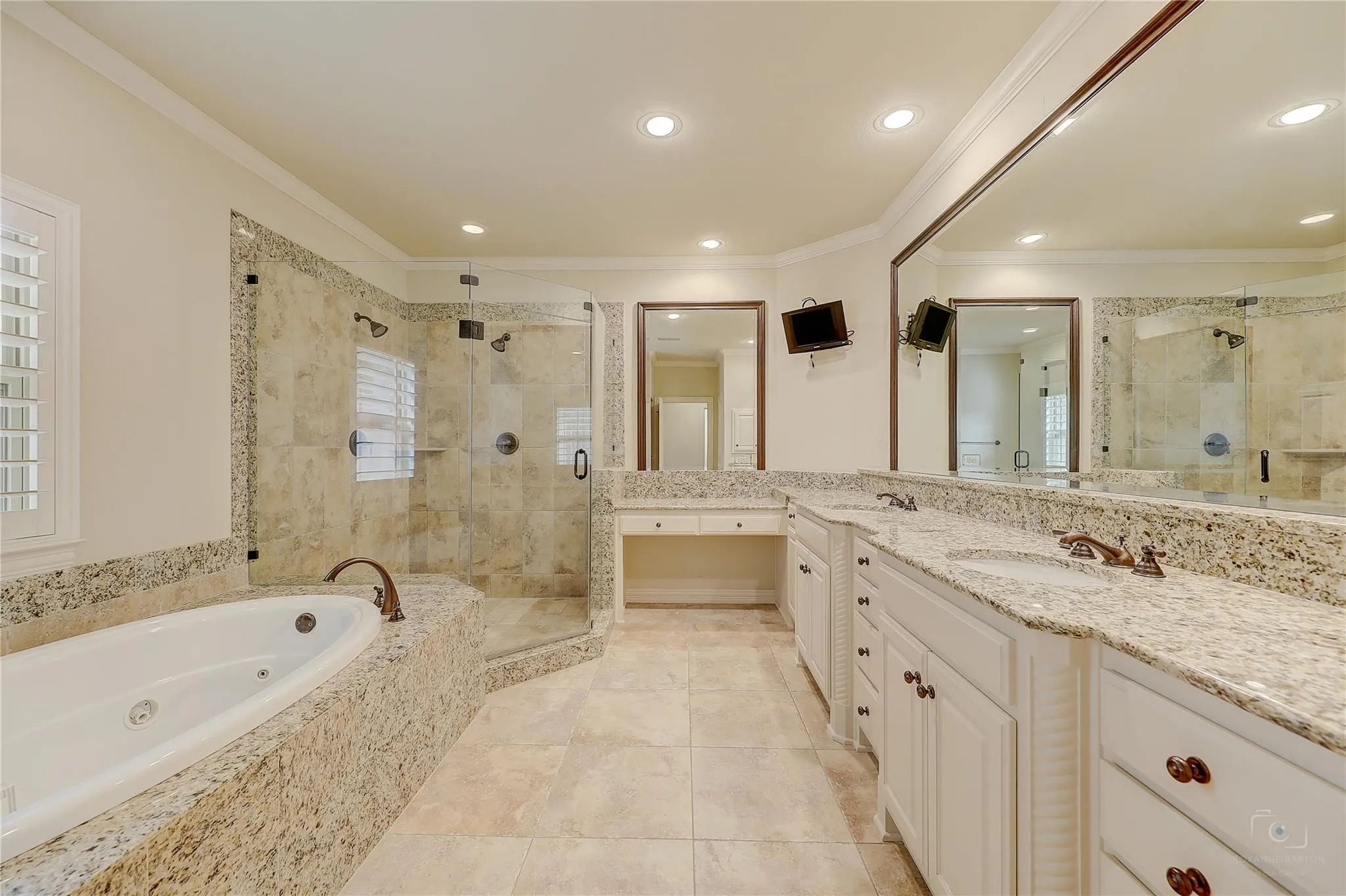 Freestanding bathtub with integrated jets, walk-in shower with glass enclosure, dual vanity with granite countertops, light wood-finish cabinetry, and recessed lighting