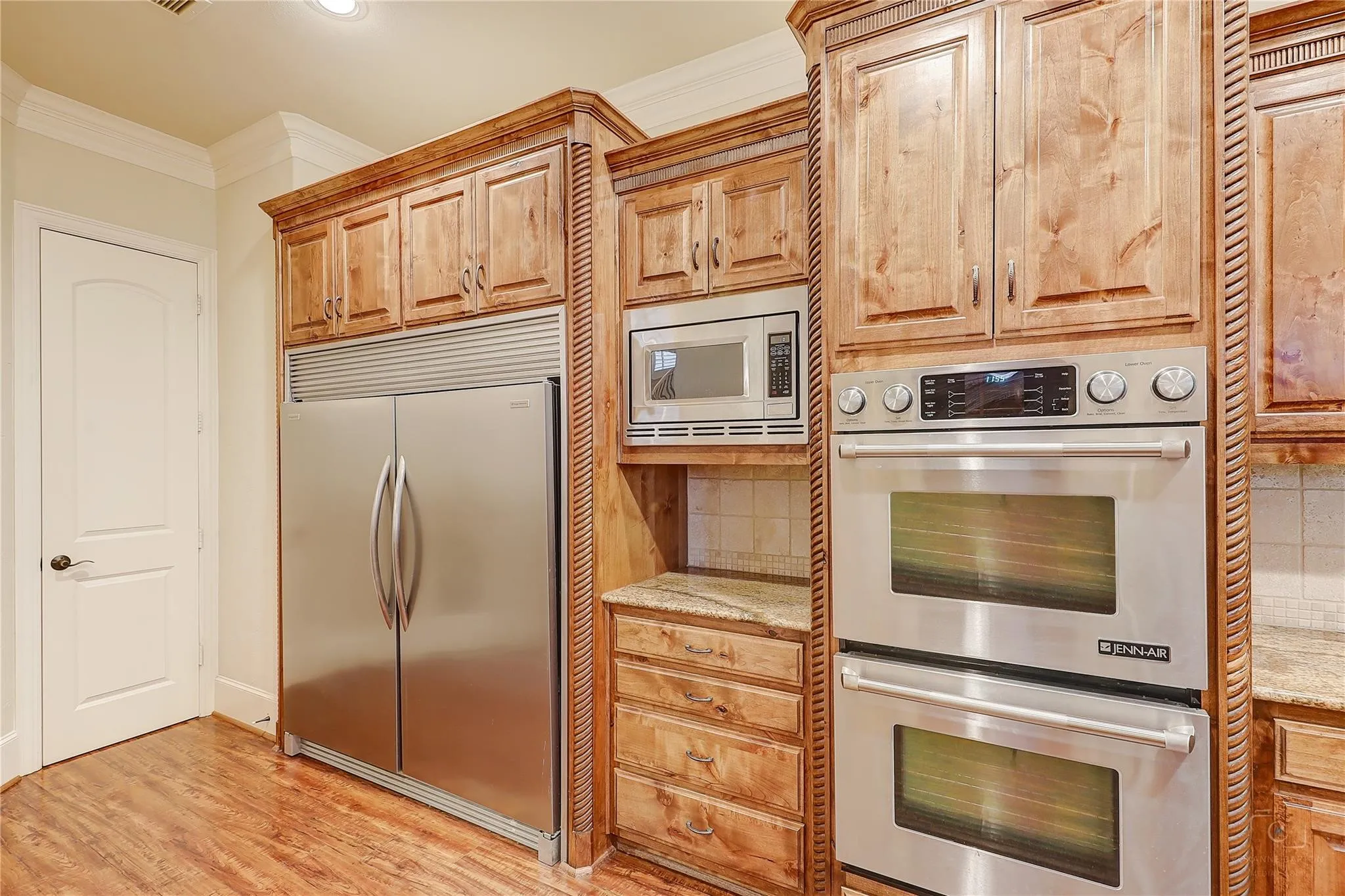 Integrated stainless steel refrigerator, built-in microwave, double wall ovens, wood-finish flooring, and crown molding