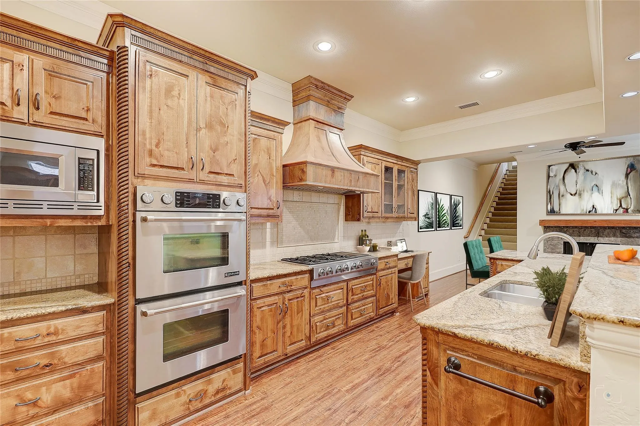 Kitchen featuring wood-finish flooring, custom wood cabinetry, stainless steel double ovens, a built-in microwave, and stone countertops