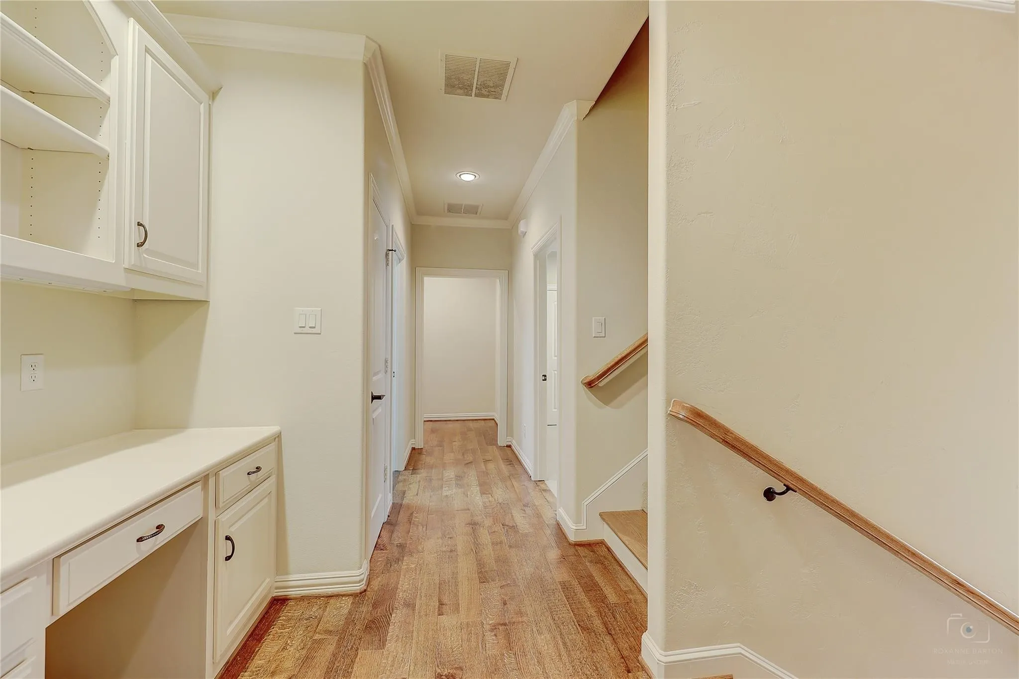 Wood-finish flooring throughout, built-in desk with cabinetry, light-colored walls, recessed lighting, and a staircase with a wood handrail