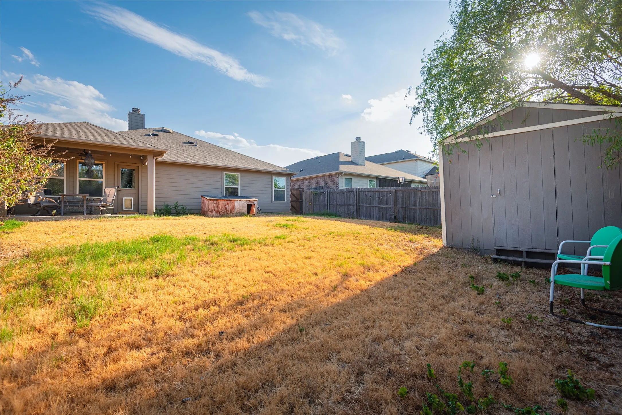 Expansive backyard featuring a gray storage shed, privacy fencing, and a covered patio