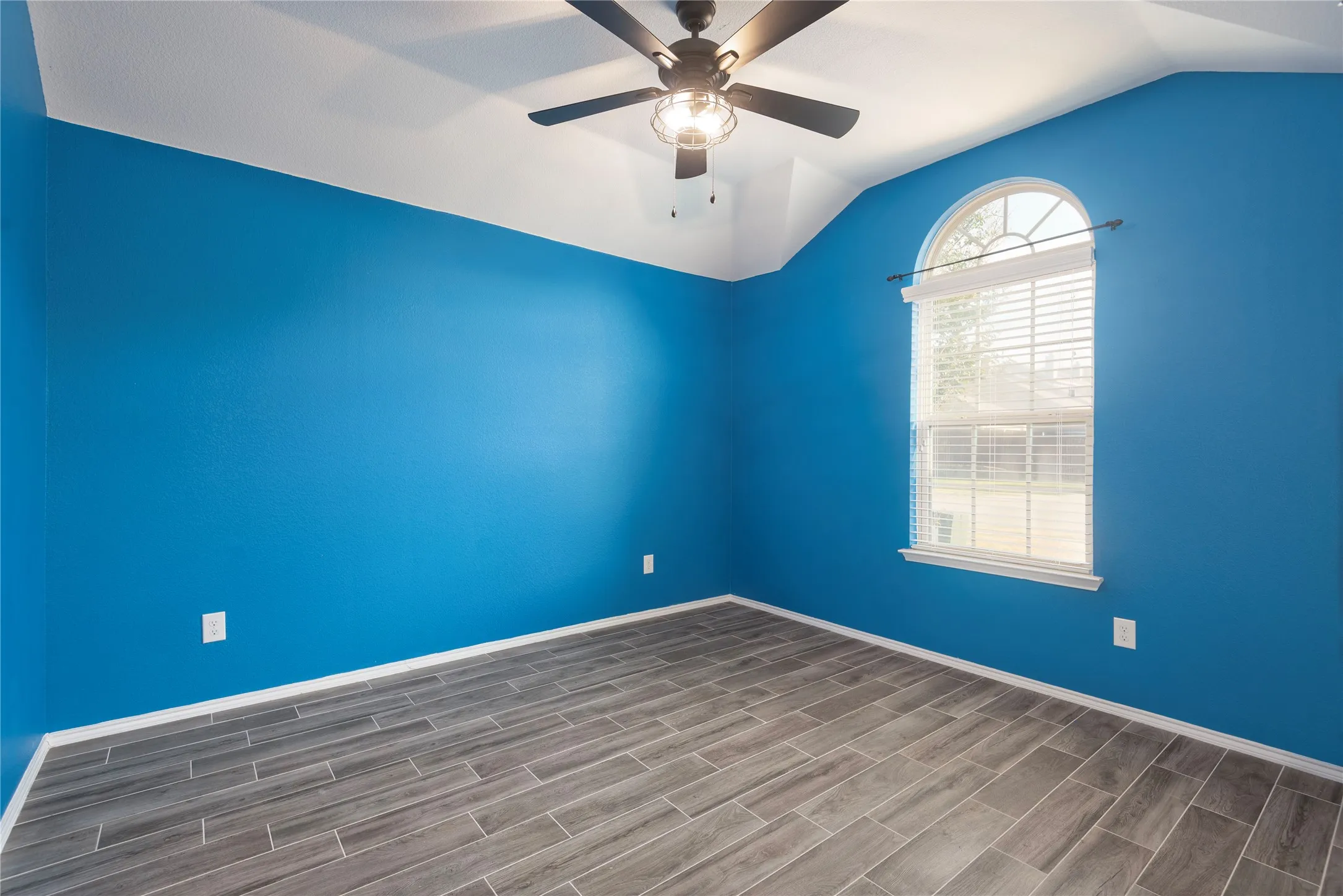 Vaulted ceiling with a ceiling fan, wood-finish flooring, and an arched window with blinds