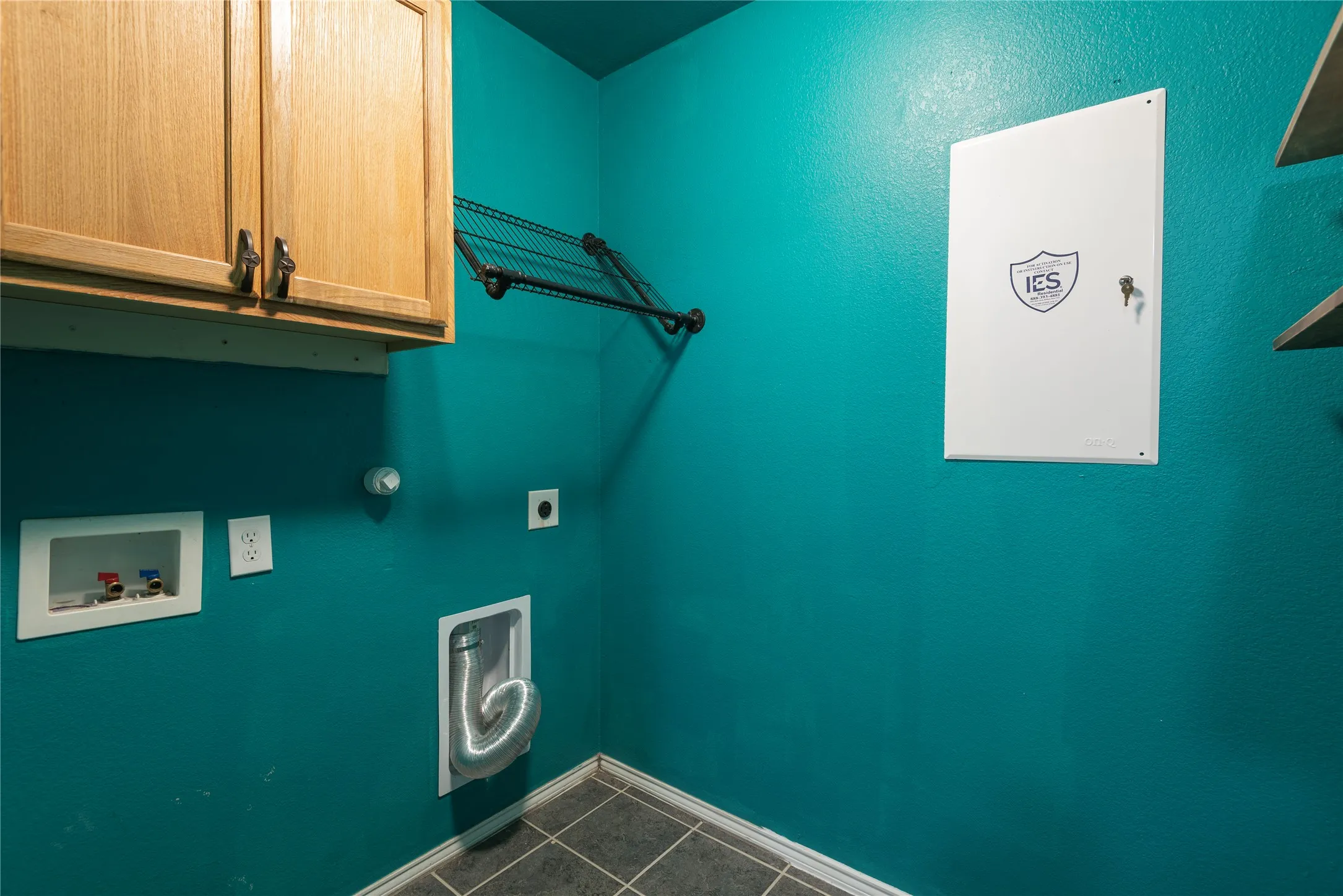 Utility room featuring vibrant turquoise walls, wood-finish cabinetry, slate-look tile flooring, and multiple electrical outlets and fixtures for convenient access and functionality