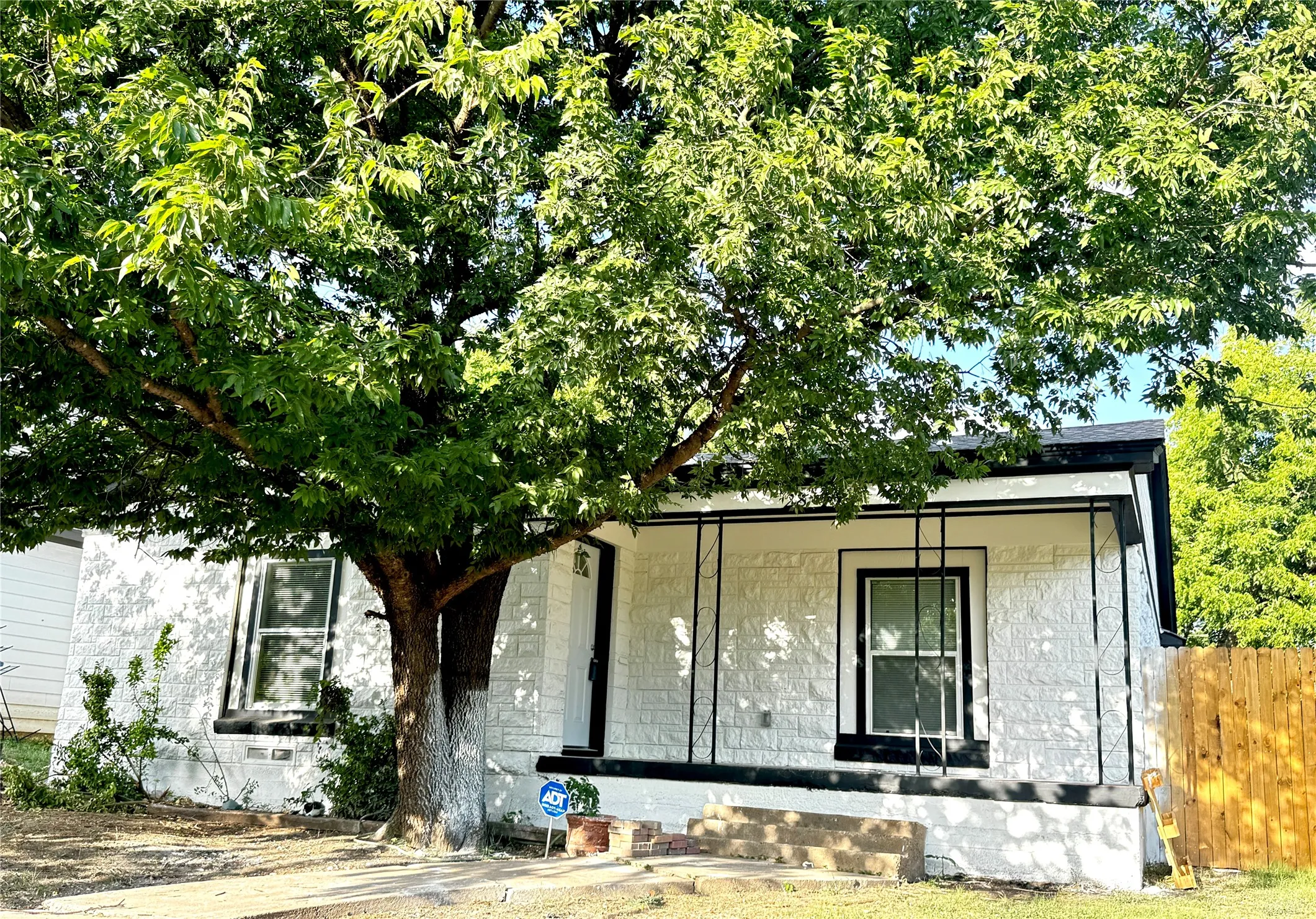 White brick exterior with black trim windows, a covered front porch, and a mature shade tree