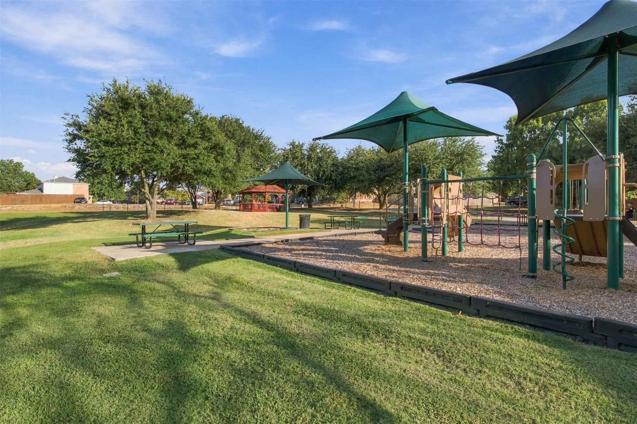 Expansive green space featuring a playground with shade structures, a picnic area, and a red gazebo
