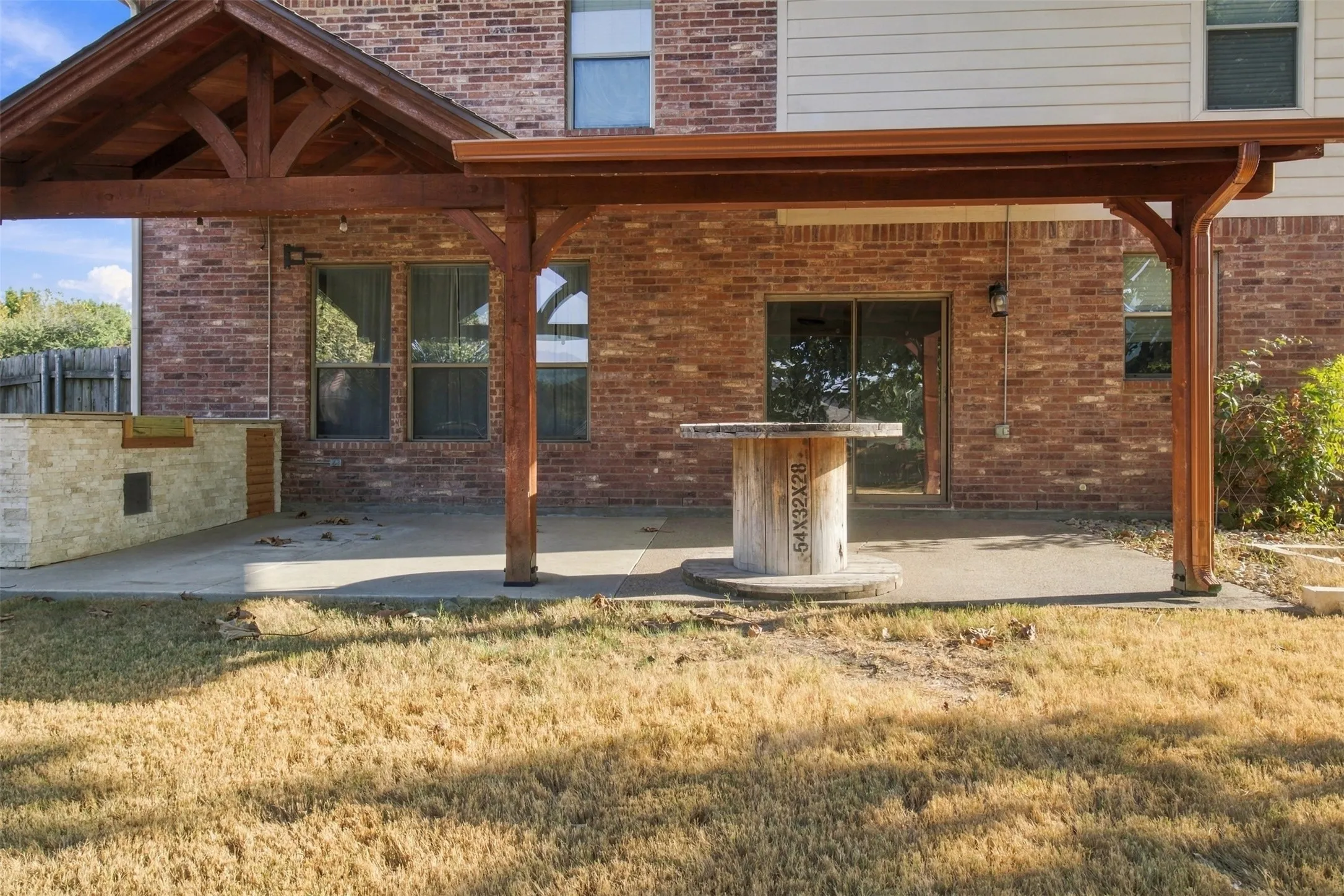 Expansive concrete patio featuring a wood pergola, built-in stone-clad outdoor kitchen, and direct access to interior via sliding glass doors