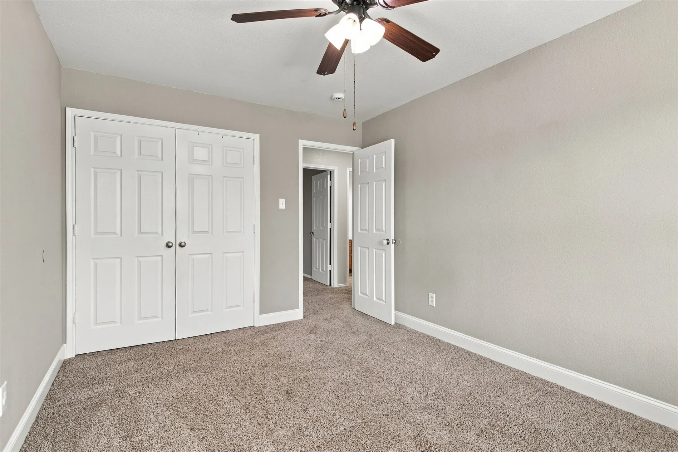 Neutral tone wall paint, textured carpeting, white trim, paneled interior doors, and a ceiling fan with integrated lighting