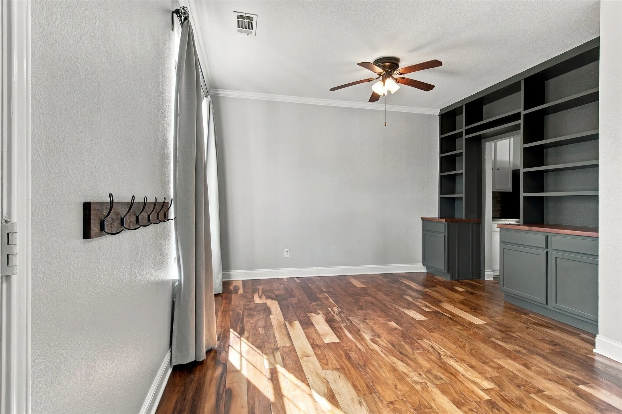 Wood-finish flooring, built-in shelving, built-in cabinetry, ceiling fan with integrated lighting, and crown molding
