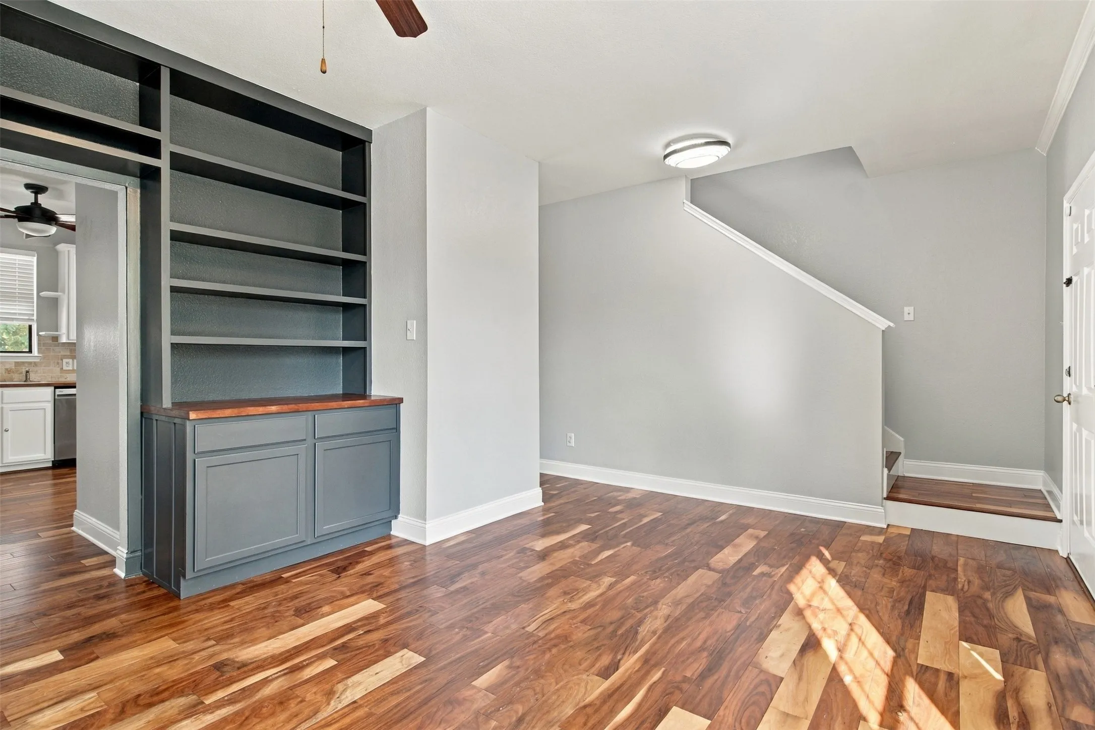 Built-in shelving unit with lower cabinetry, wood-finish flooring, staircase, and ceiling fan