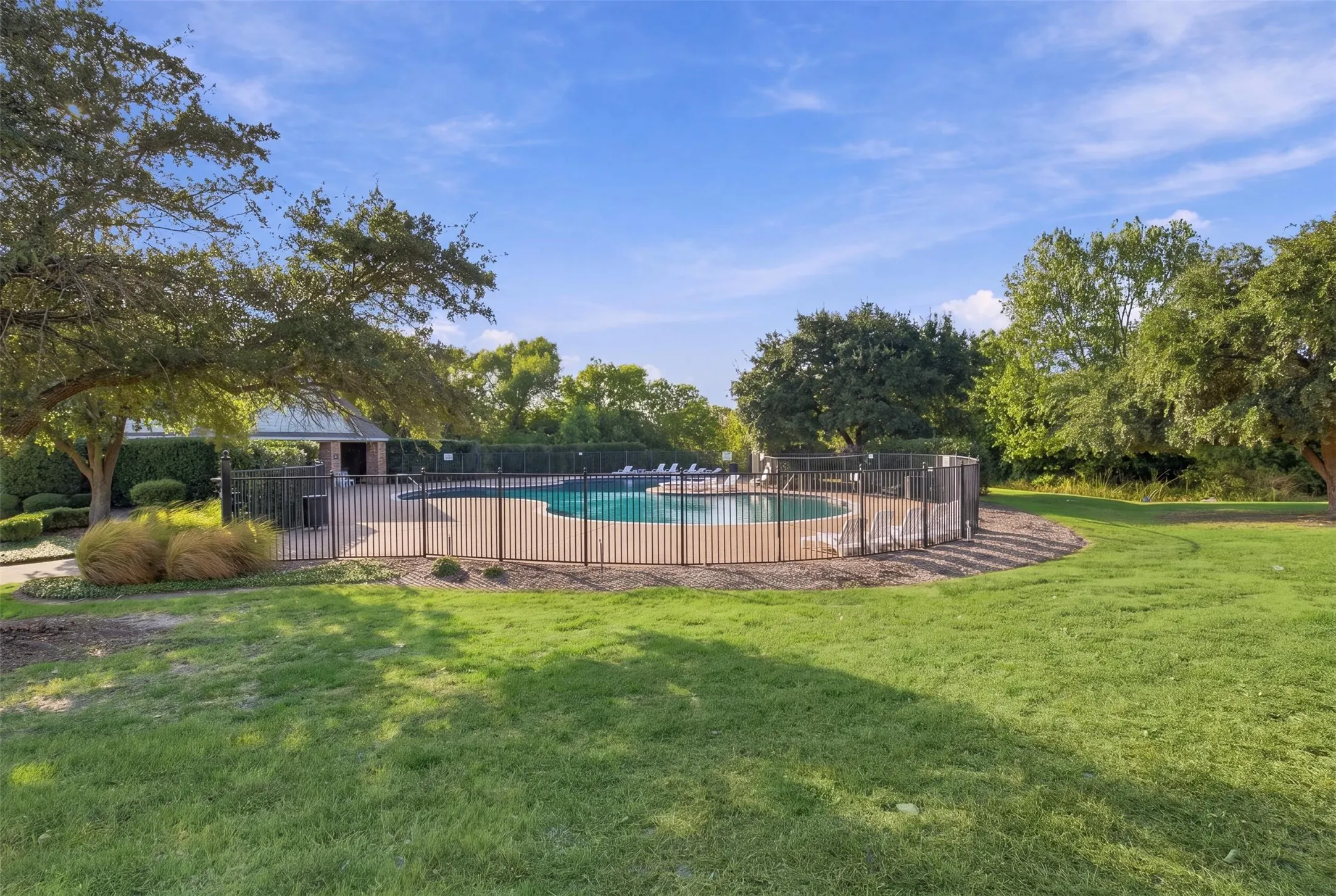 Outdoor swimming pool with surrounding black metal fencing, paved pool deck, and adjacent covered structure