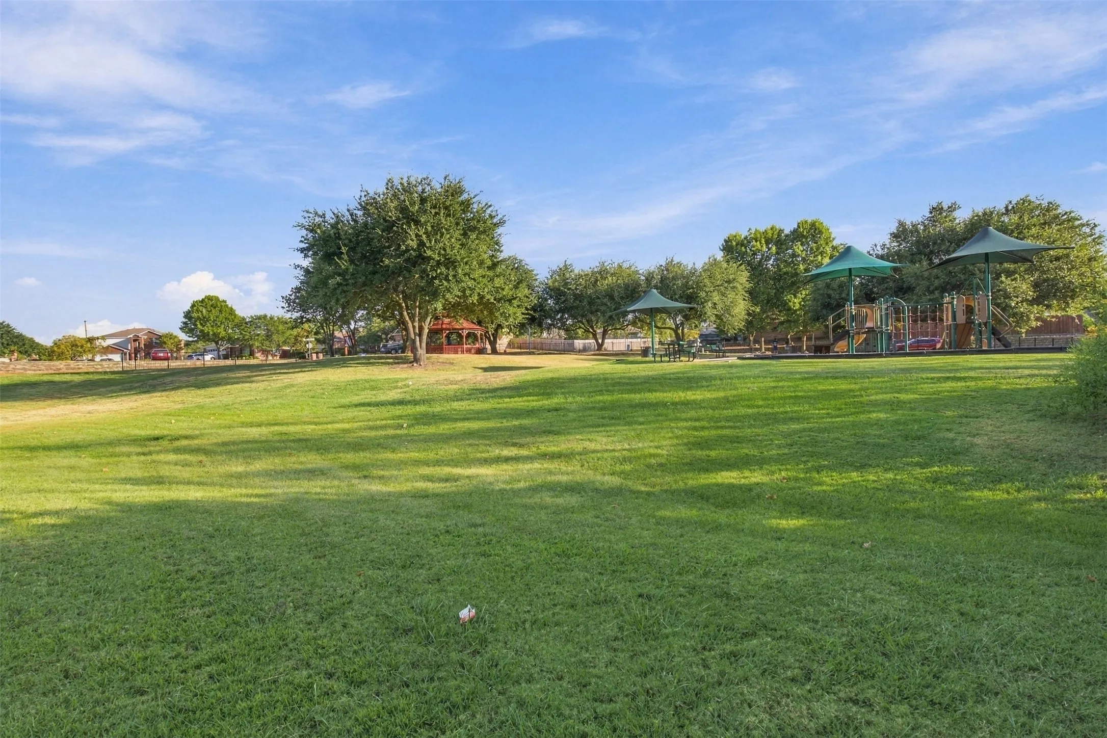 Expansive green space featuring a playground structure with multiple slides, a covered picnic area, and mature trees