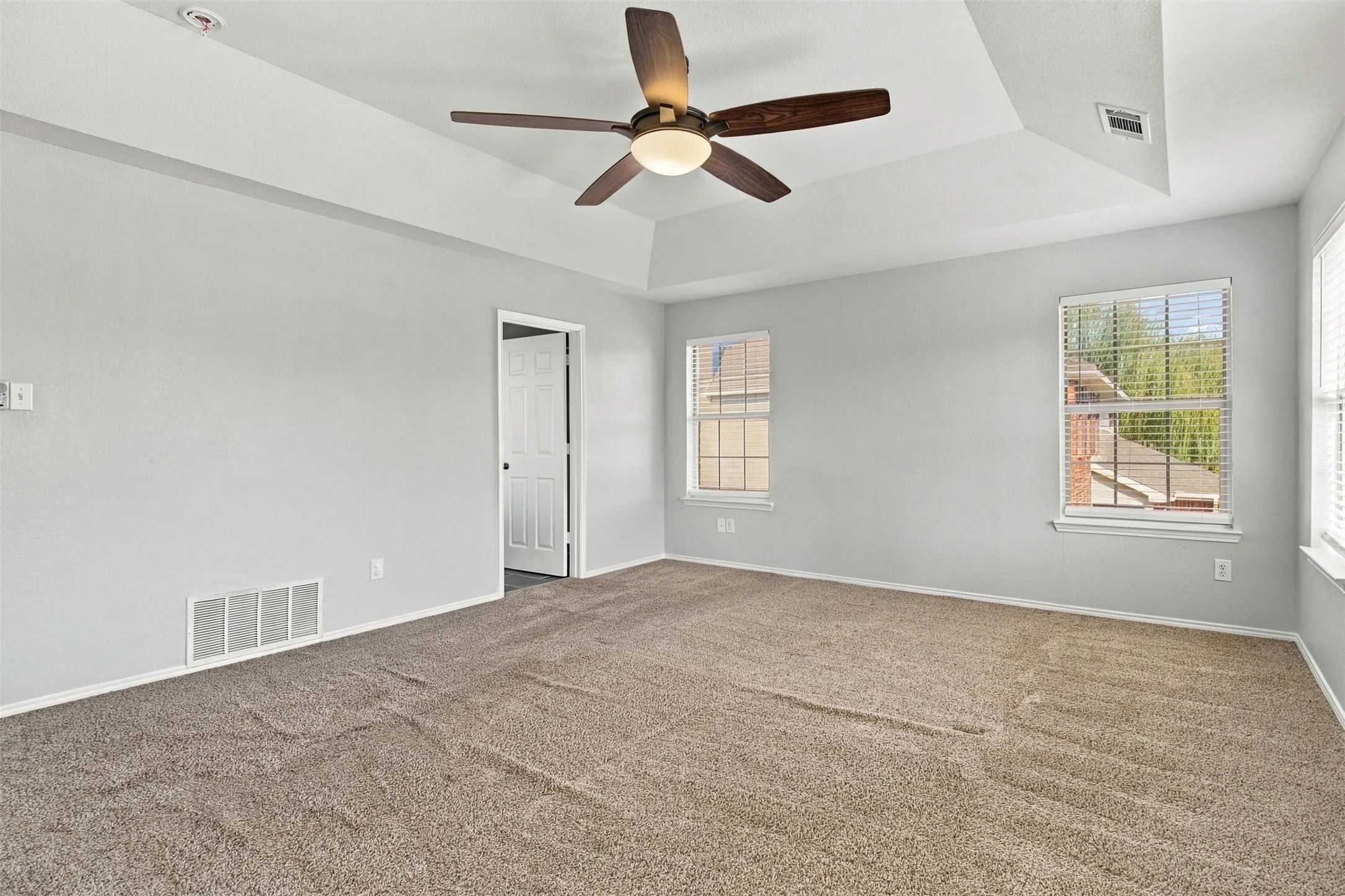 Tray ceiling with a ceiling fan, two windows, and neutral wall paint