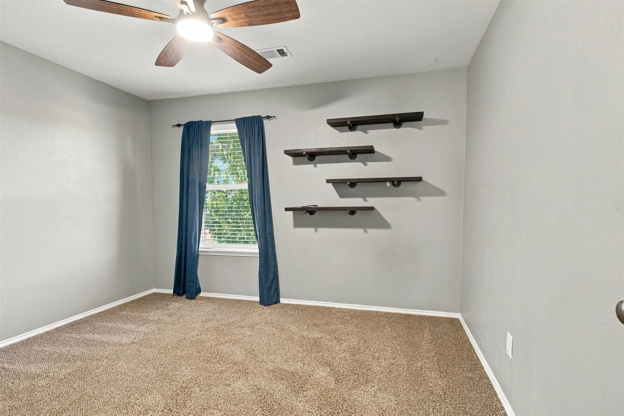 Neutral wall paint, carpet flooring, a ceiling fan with light fixture, and built-in wall shelving