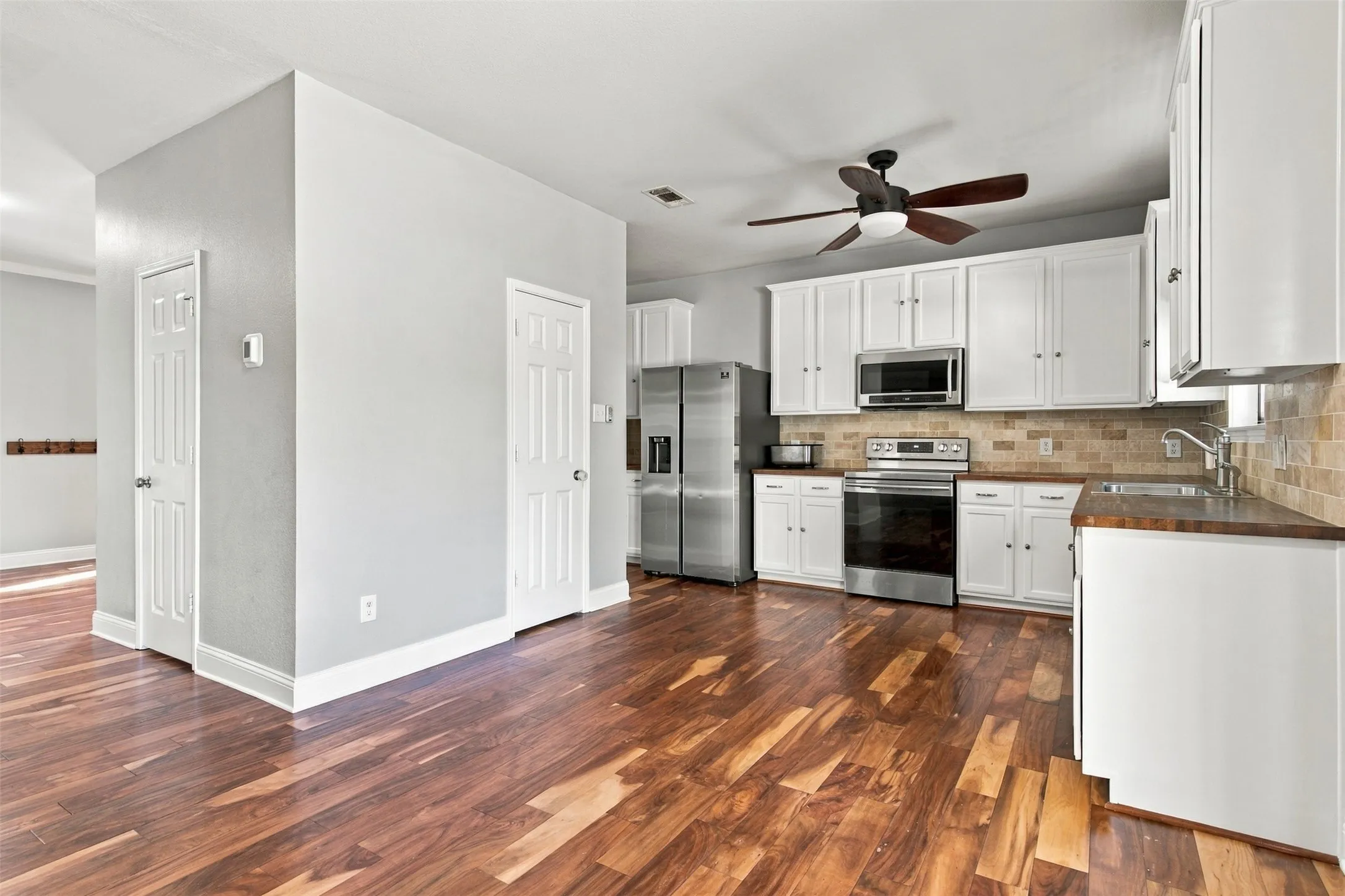 Kitchen with wood-finish flooring, white cabinetry, stainless steel appliances, and a tiled backsplash