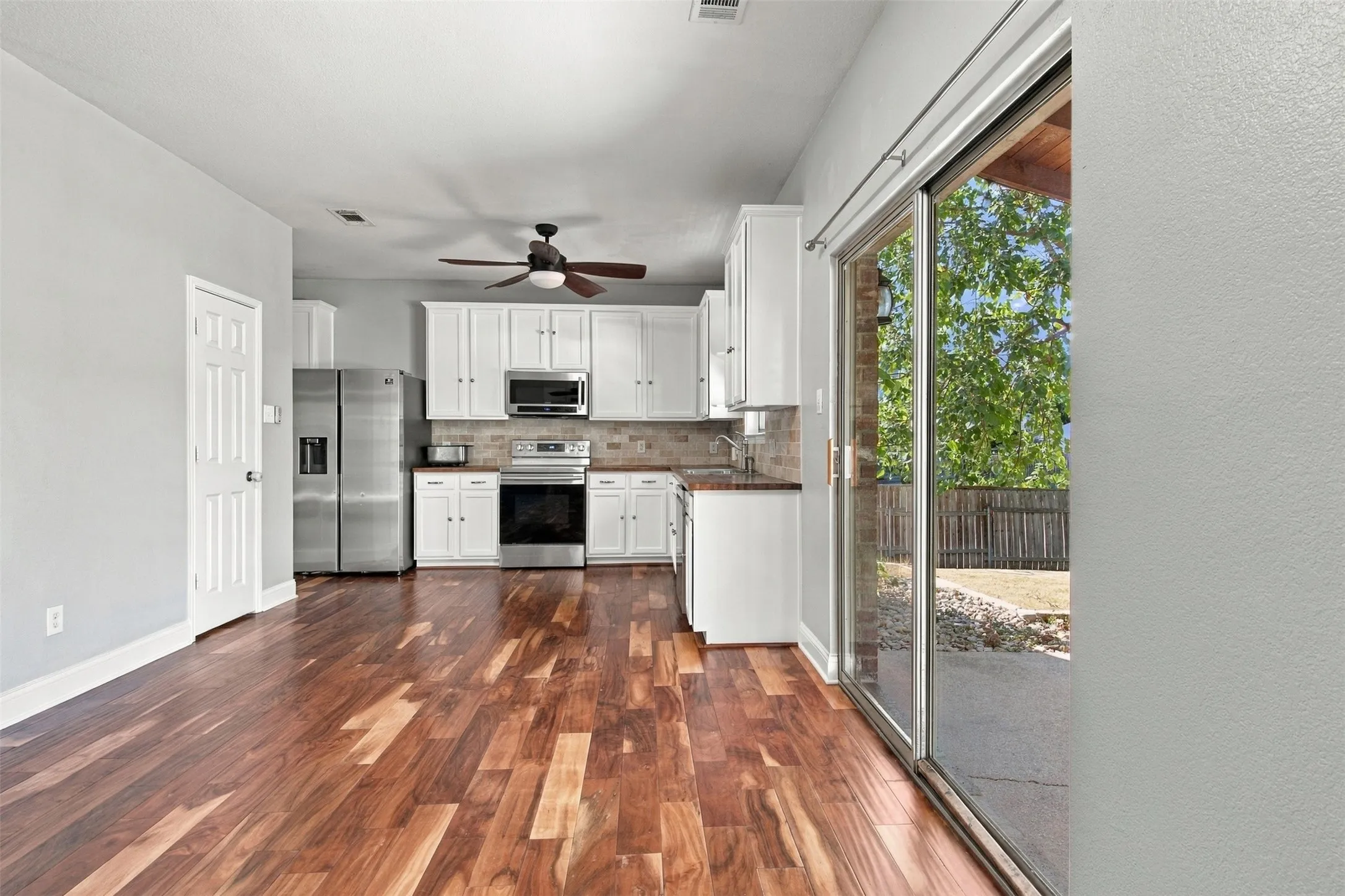 Wood-finish flooring throughout, kitchen with white cabinetry, stainless steel appliances, and a tiled backsplash
