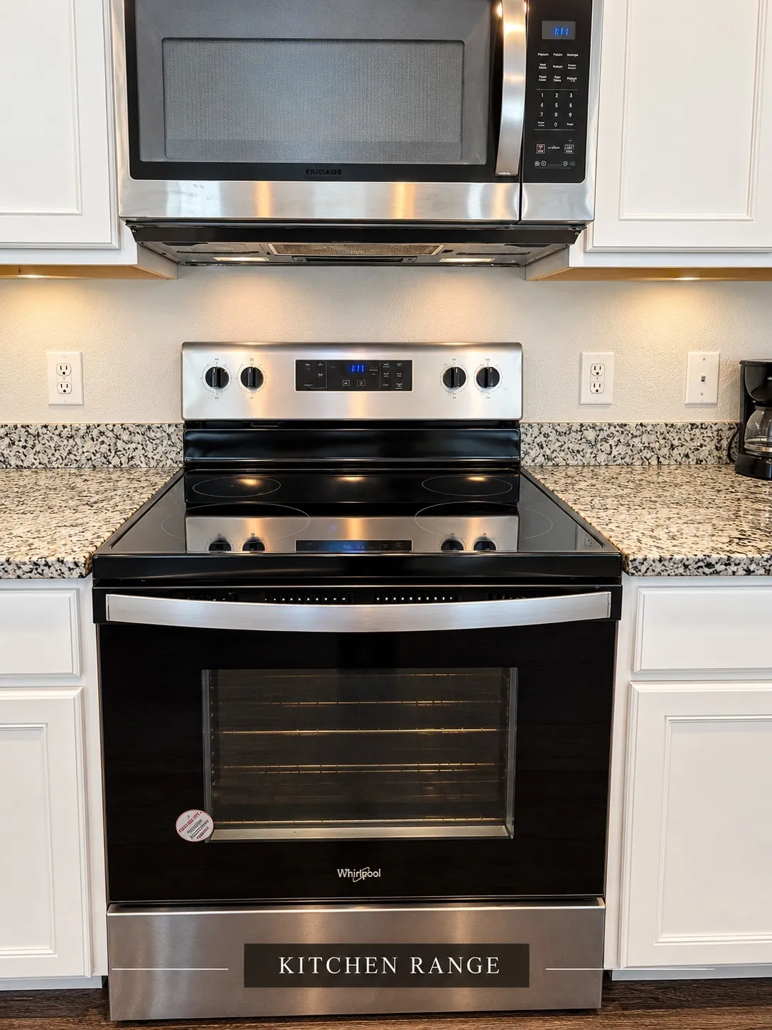 Stainless steel range with a smooth cooktop, coordinating microwave, granite-style countertops, white cabinetry, and under-cabinet lighting