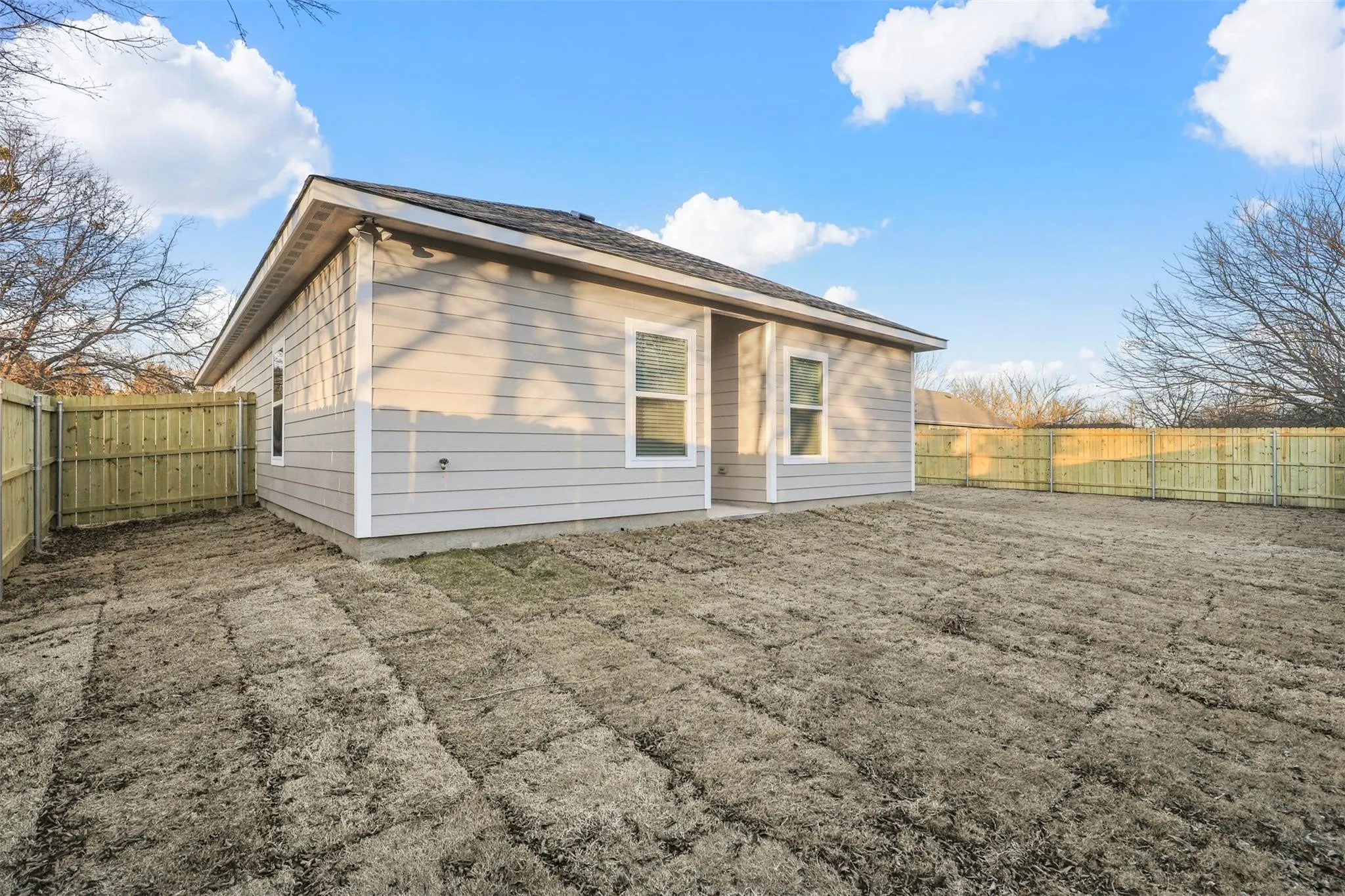 Rear exterior featuring horizontal siding, white trim accents, a sloped roofline, and a privacy fence