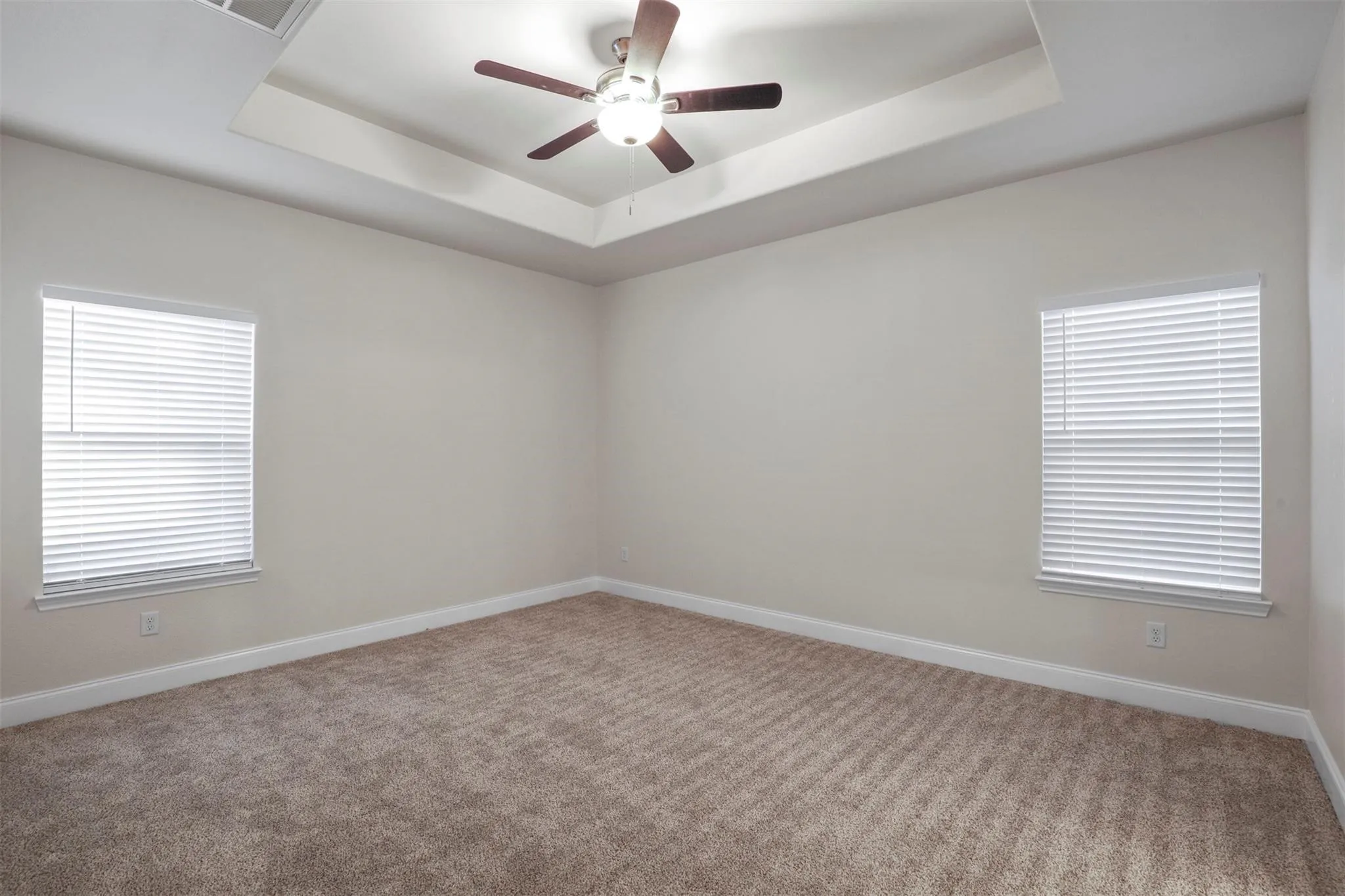 Tray ceiling with a ceiling fan light fixture, two windows, and neutral carpeting