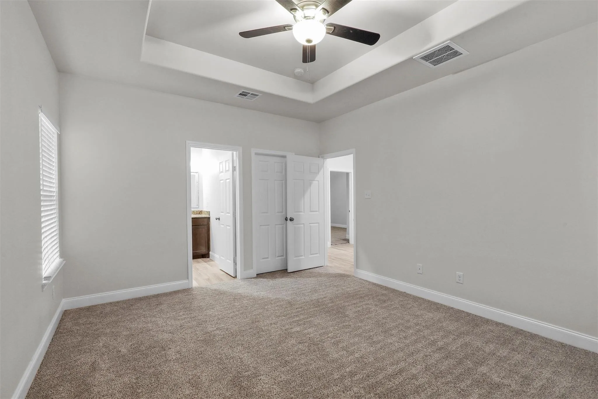 Recessed ceiling with a central fan light fixture, neutral carpet flooring, and a window with horizontal blinds