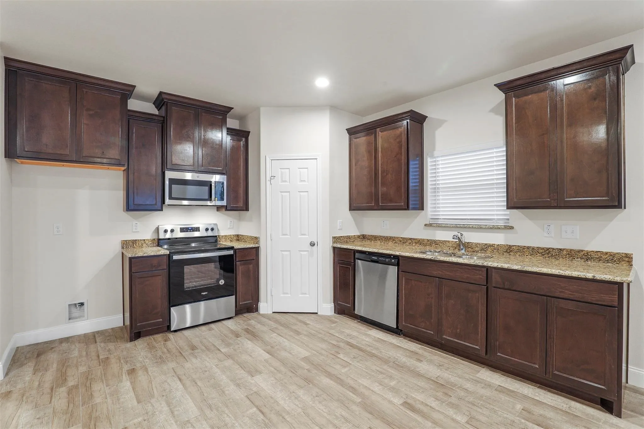 Kitchen featuring wood-finish flooring, dark wood cabinetry, granite countertops, and stainless steel appliances