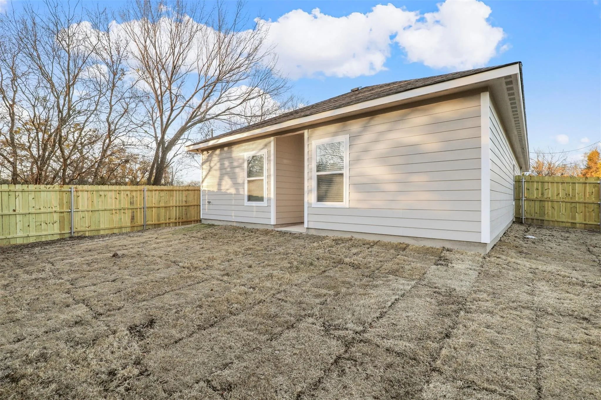 Exterior featuring light-colored siding, a dark shingle roof, a window, and a wood privacy fence