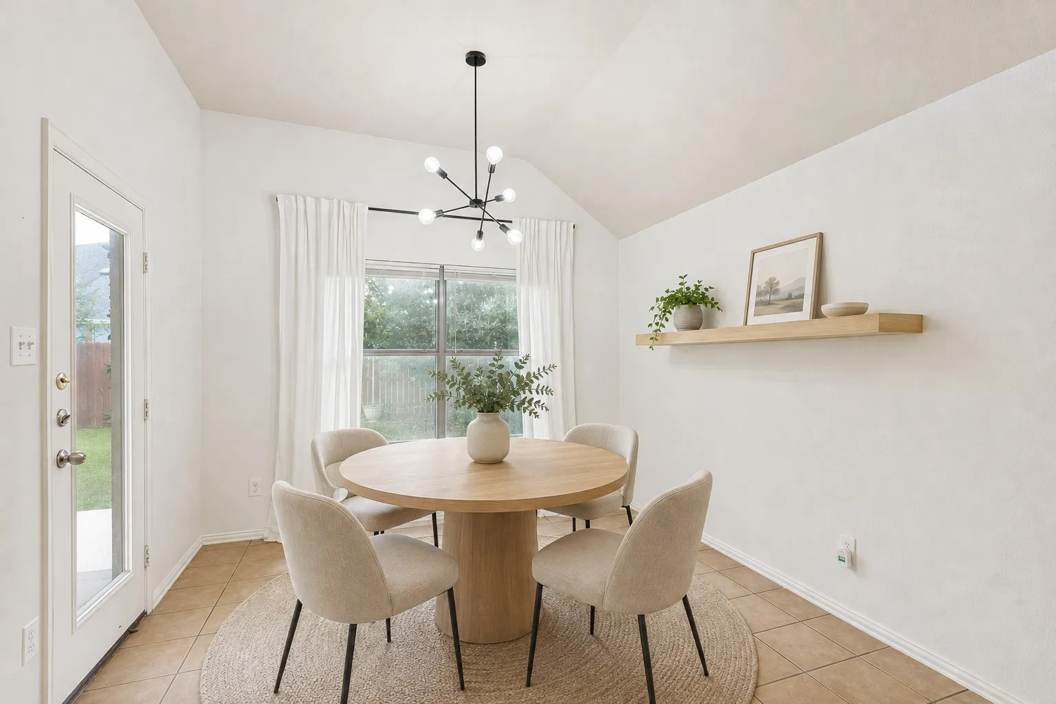 Vaulted ceiling with a modern black sputnik chandelier, full-light exterior door, large window with curtain rod, wood-finish floating shelf, and tile flooring