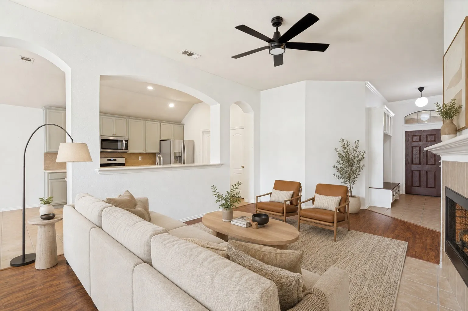 Wood-finish flooring throughout, featuring a living area with a ceiling fan, fireplace with a tile surround, and arched wall openings