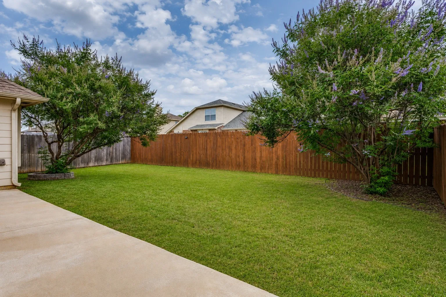 Expansive green lawn with mature trees, surrounded by a wood privacy fence