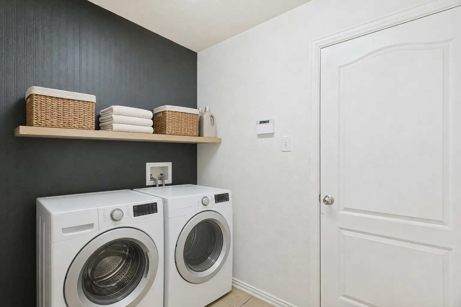 Dedicated laundry area featuring a wood-finish floating shelf, dark accent wall, and white paneled door