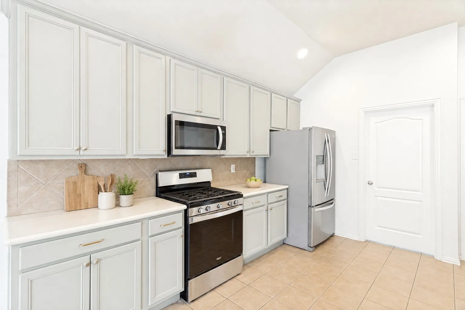 Kitchen with light-toned cabinetry, stainless steel appliances, tile backsplash, light-colored countertops, and tiled flooring