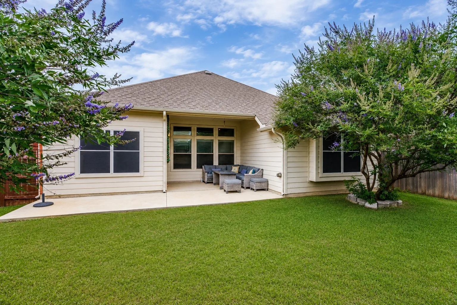 Expansive backyard featuring a manicured lawn, established trees, and a concrete patio