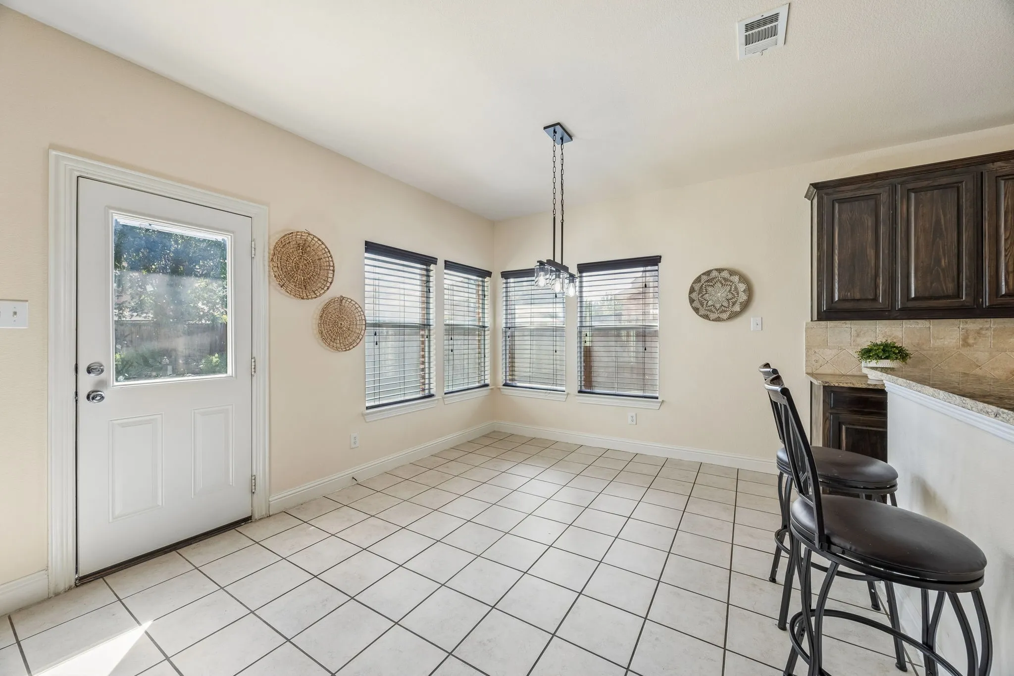 Light-colored tile flooring, multiple windows with blinds, a glass-paneled exterior door, and a kitchen counter with dark cabinetry and a tile backsplash