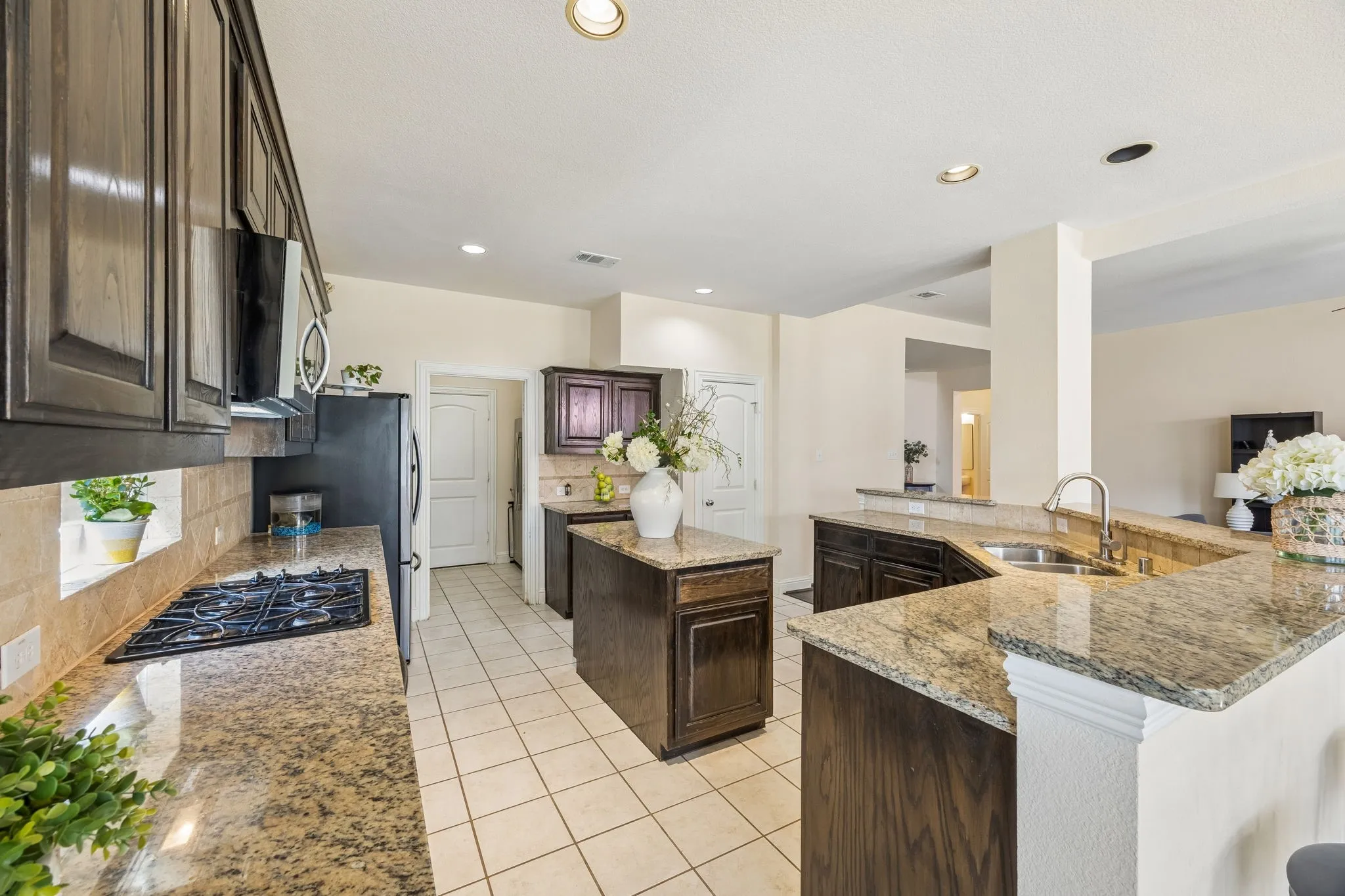 Well-appointed kitchen featuring granite countertops, dark wood cabinetry, a gas cooktop, a stainless steel sink, and recessed lighting