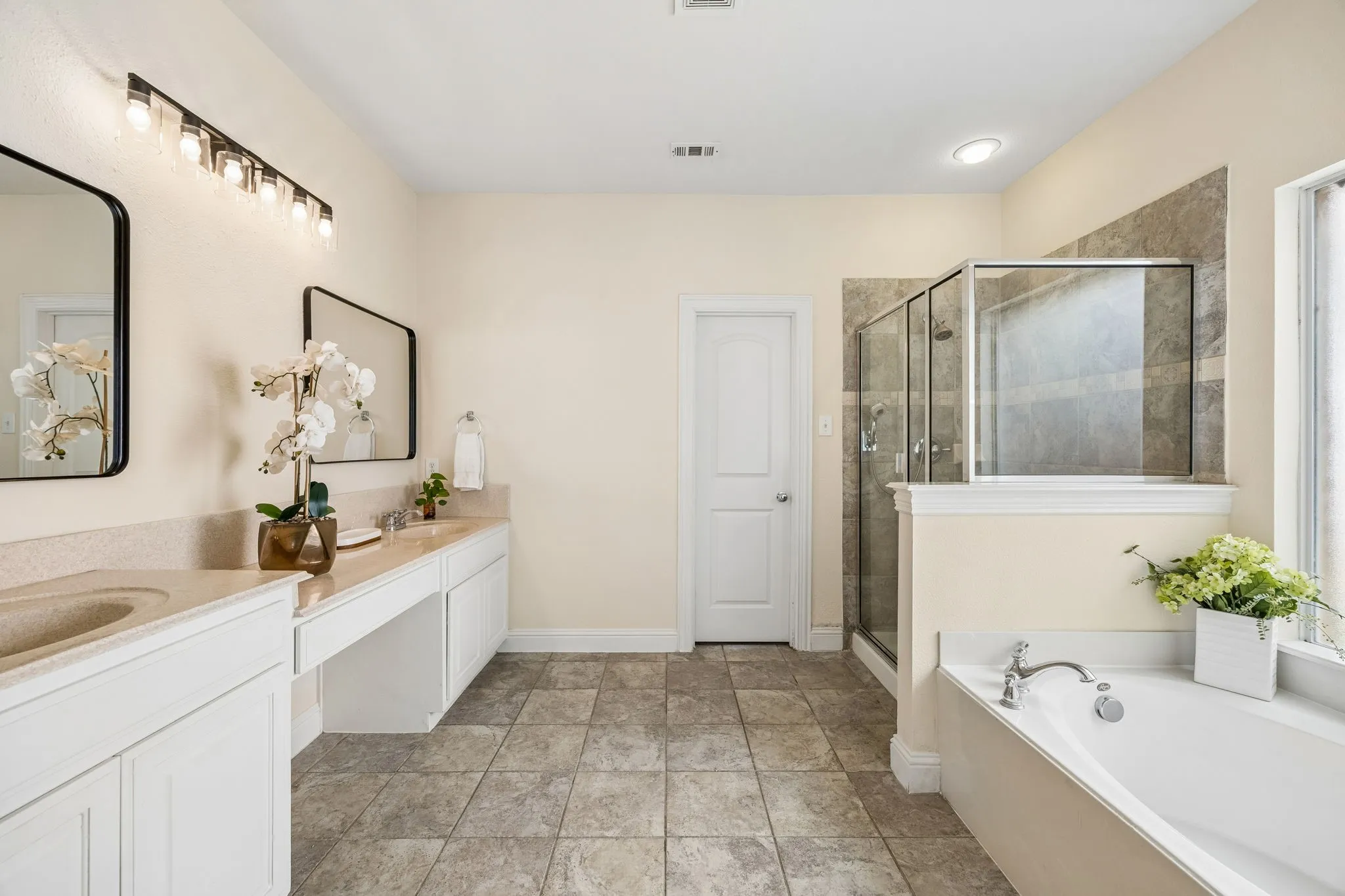 Dual vanity with integrated sinks, frameless glass shower enclosure, separate soaking tub, and tile flooring