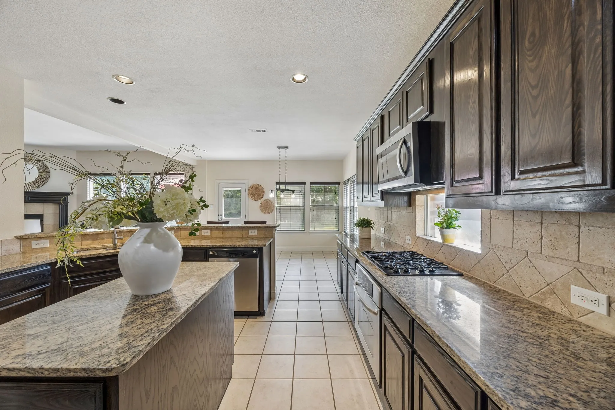 Kitchen featuring dark wood-finish cabinetry, granite countertops, a gas cooktop, tile flooring, and recessed lighting