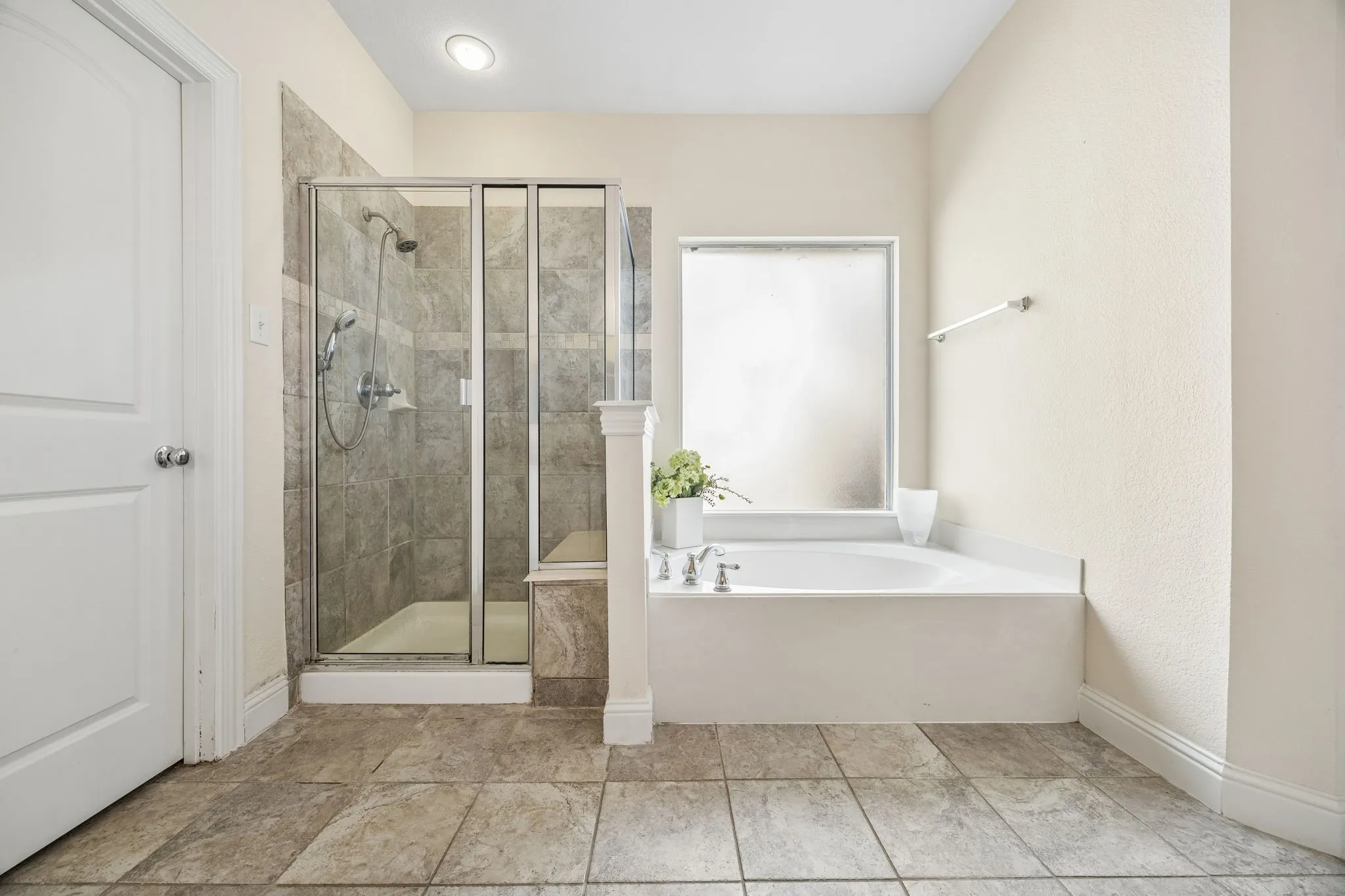 Spacious bathroom featuring an enclosed shower with full-height tile, a built-in soaking tub with a frosted window, and large format floor tiling