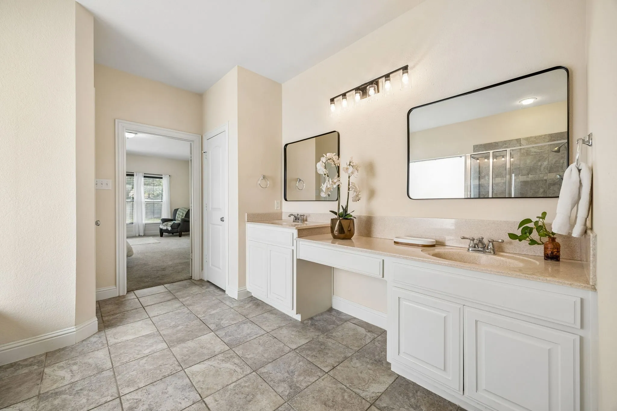 Dual vanity with integrated sinks, white cabinetry, a built-in dressing area, and tile flooring